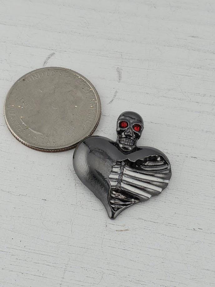 a heart-shaped brooch with a skull design, placed inside a white box.