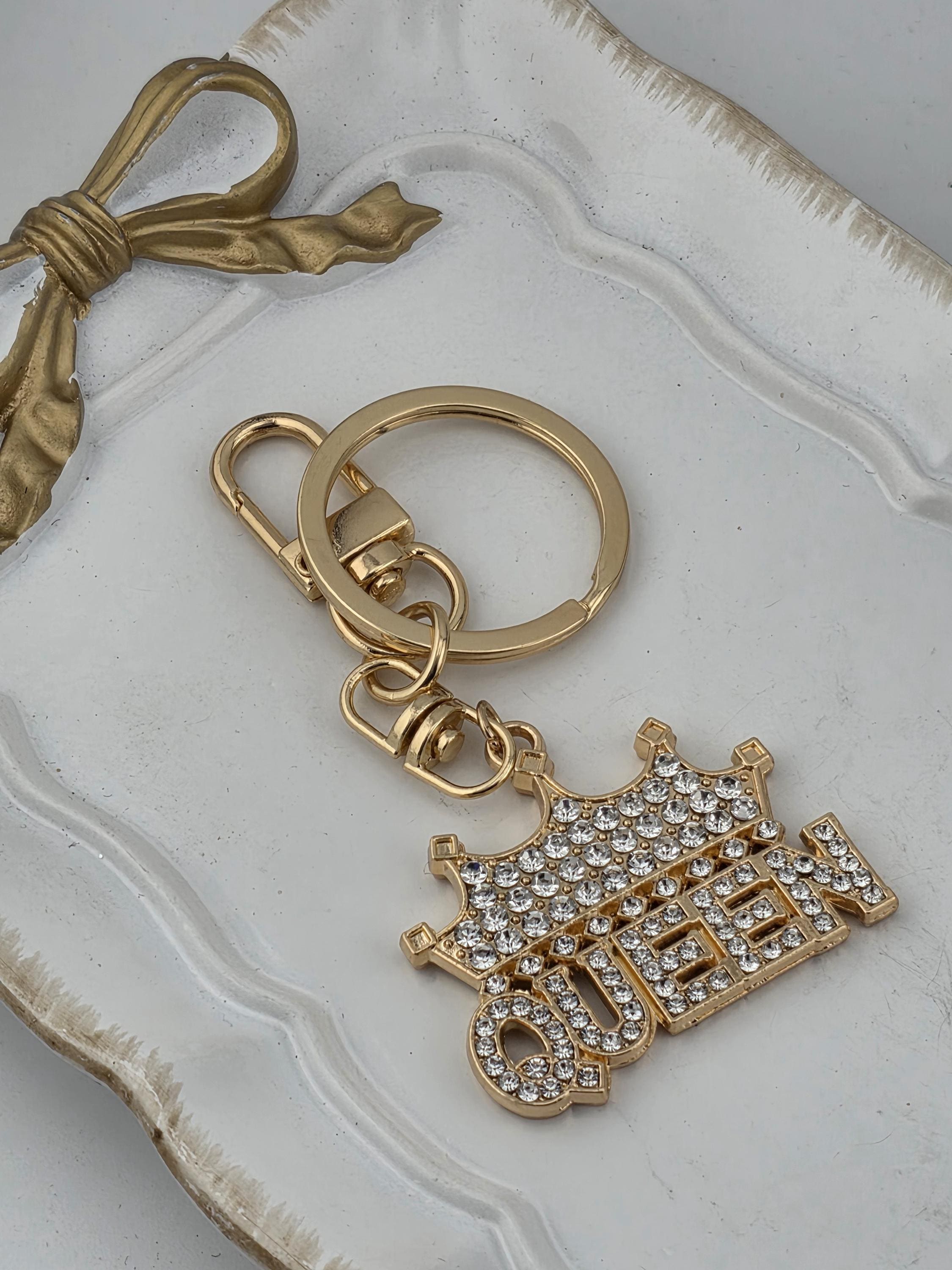 a gold keychain with a decorative charm and a gold bow on a white surface.