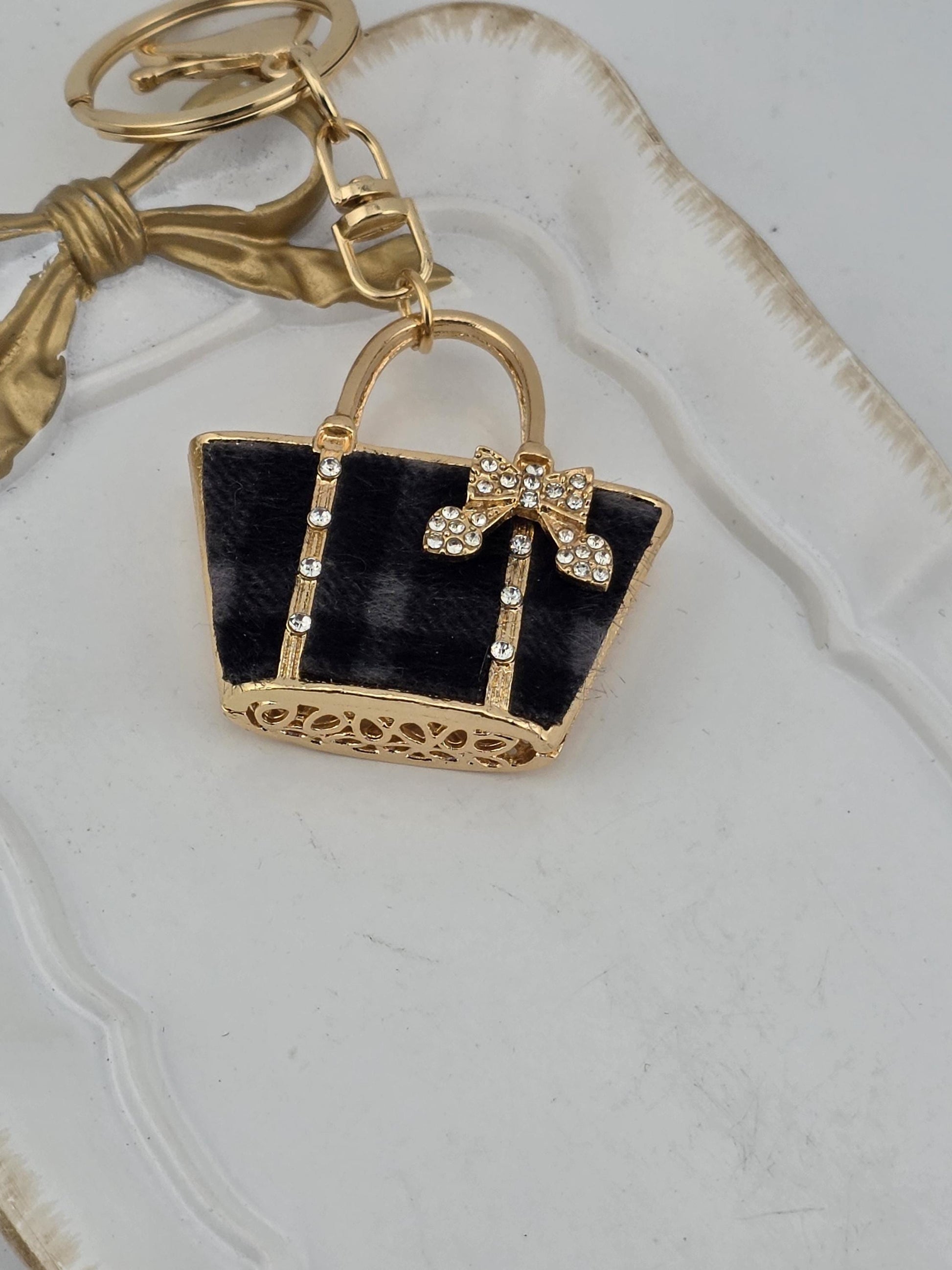A black and gold keychain with a decorative bow and a small black purse-shaped charm with a gold bow.