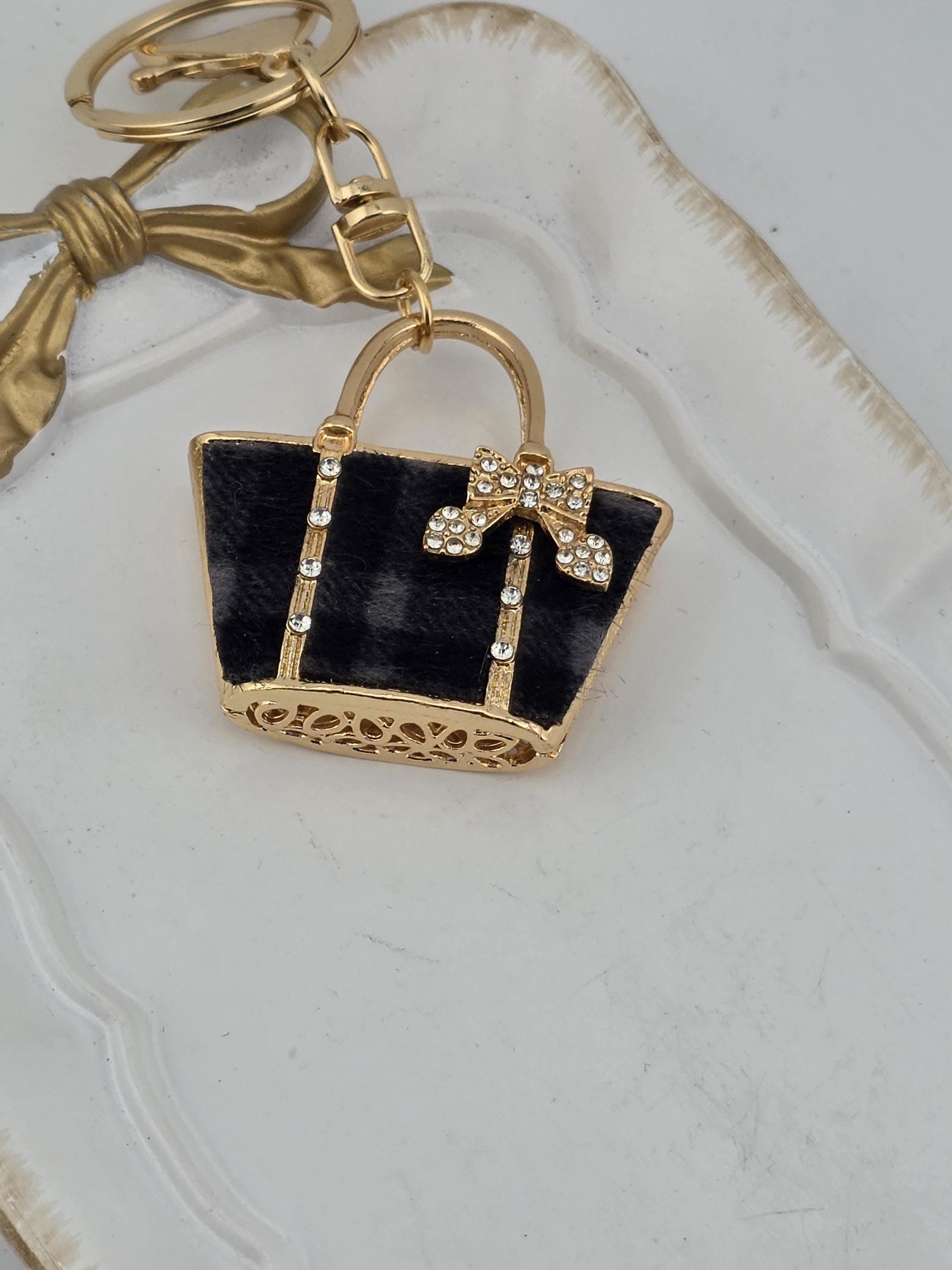 A black and gold keychain with a decorative bow and a small black purse-shaped charm with a gold bow.