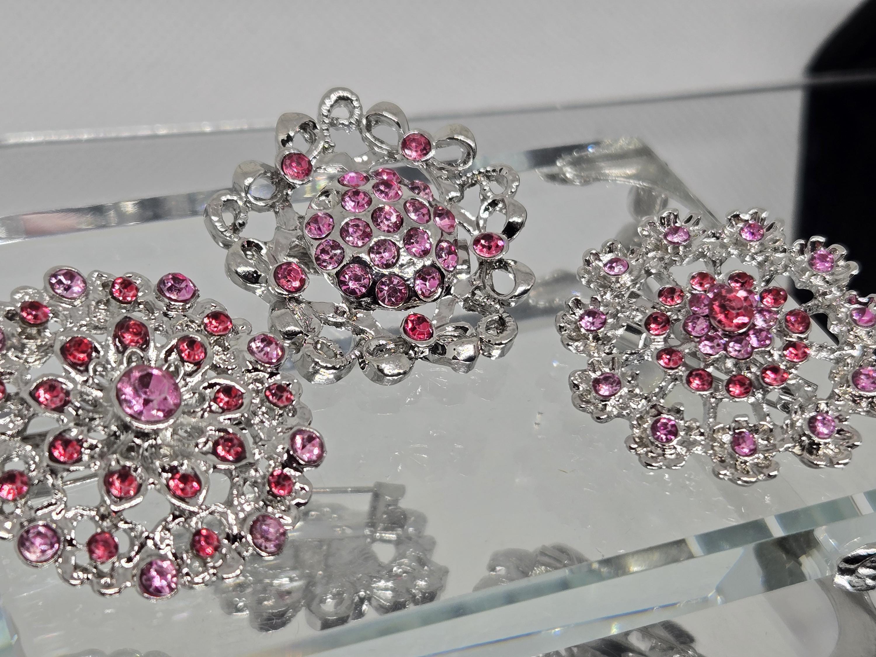 three ornate brooches with pink gemstones, displayed on a clear glass surface.