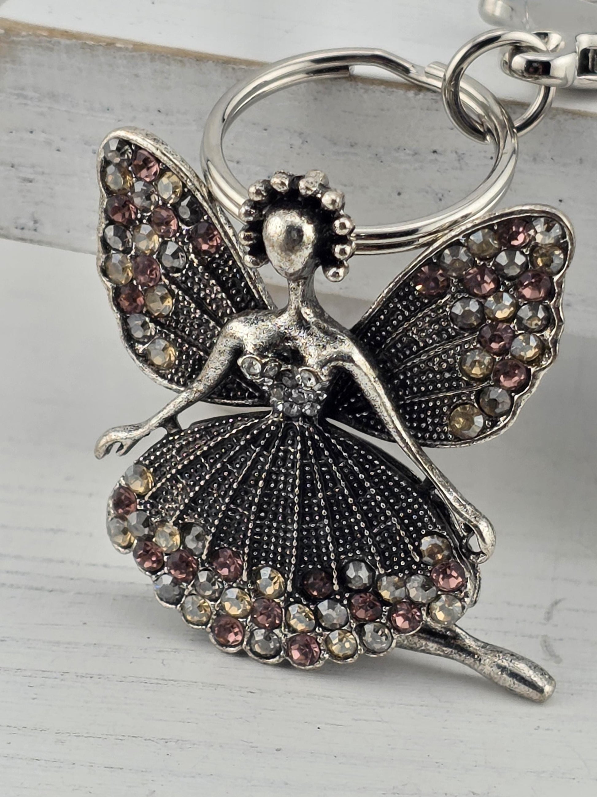 A silver-colored keychain or charm in the shape of a butterfly, adorned with colorful gemstones or jewels.