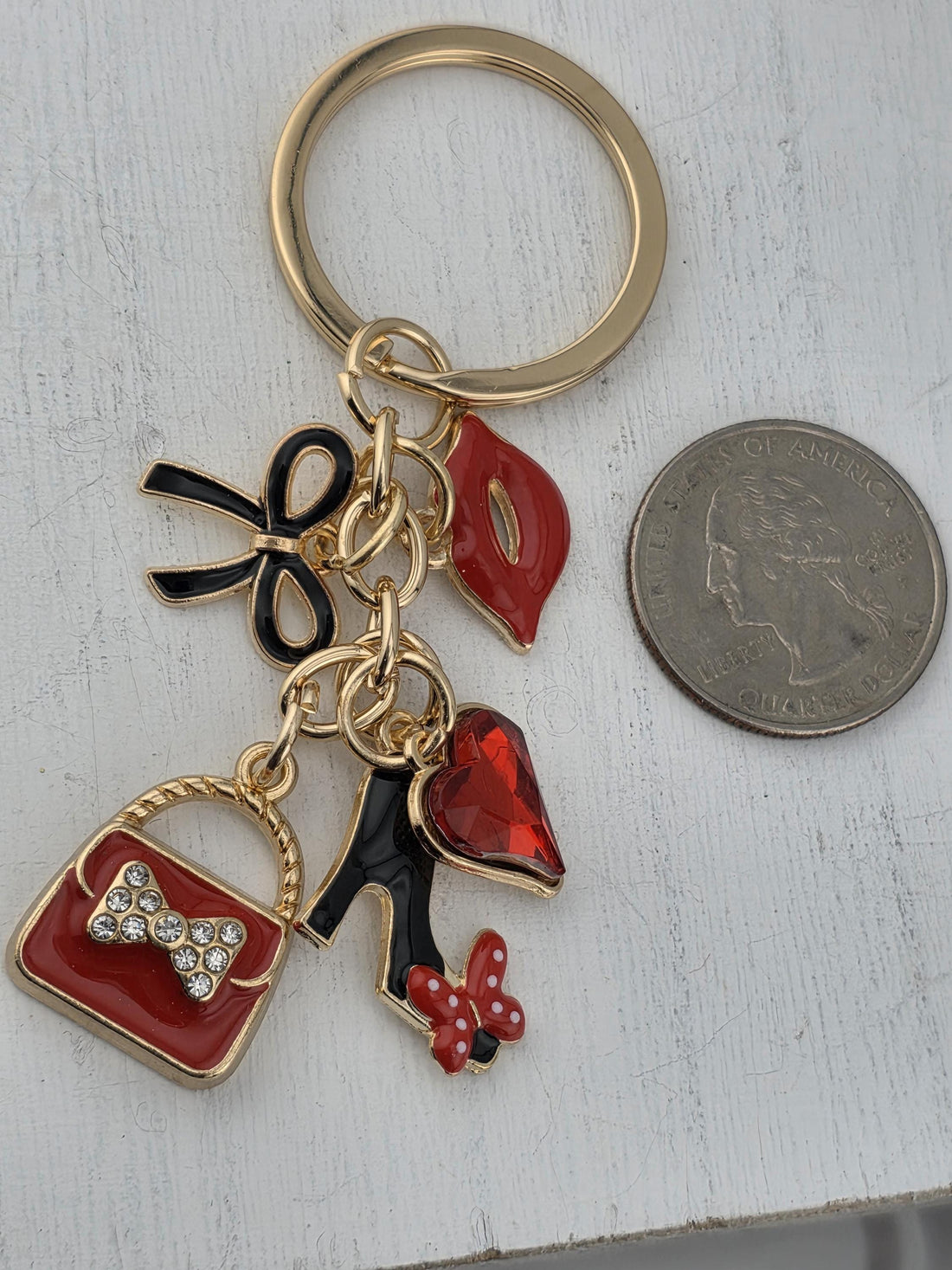 A decorative keychain with a gold frame and various colorful charms, including a red heart, a red flower, and a red bow, is displayed in a white ornate frame.