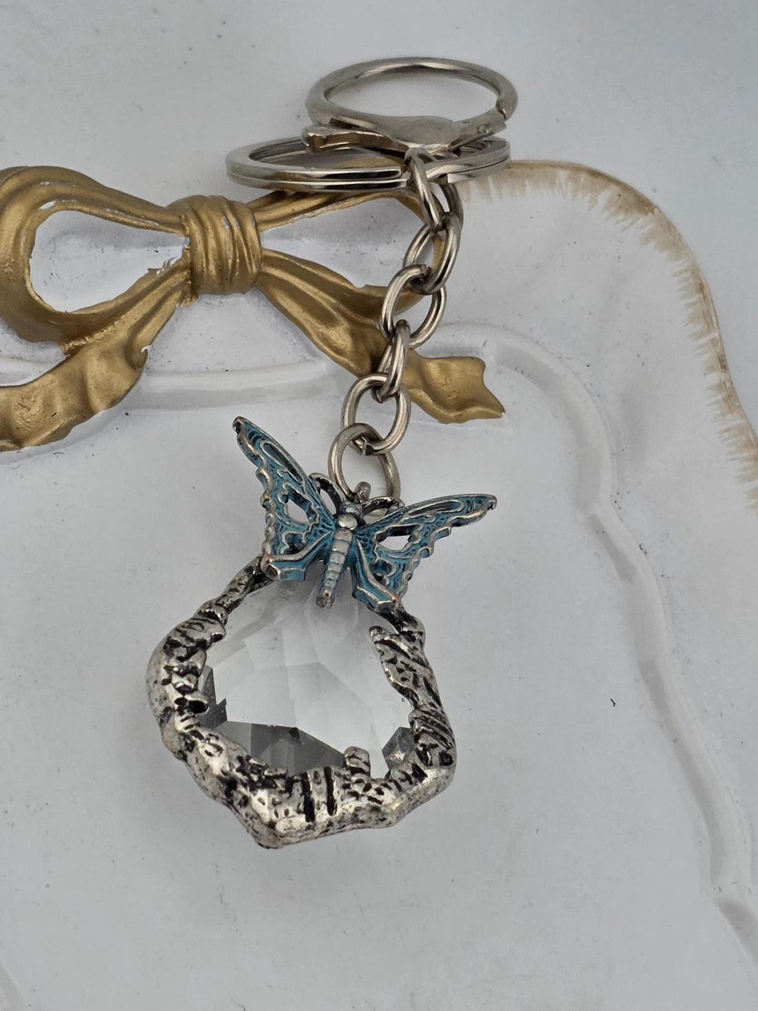 A silver-colored keychain with a clear gemstone and a butterfly-shaped charm is displayed against a black background.