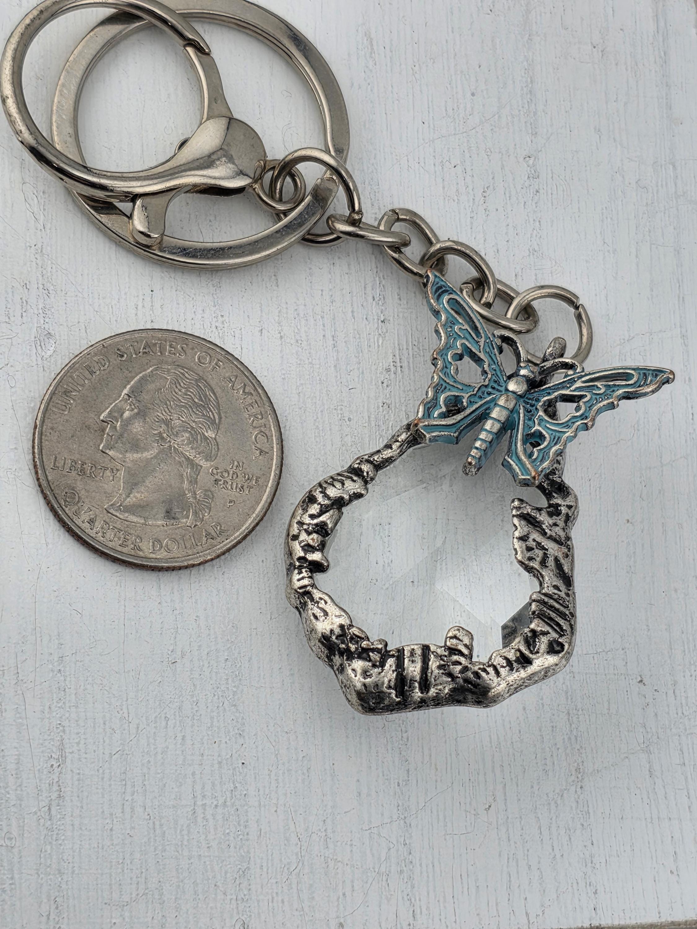 A silver keychain with a butterfly design and a small silver coin are placed on a white surface.