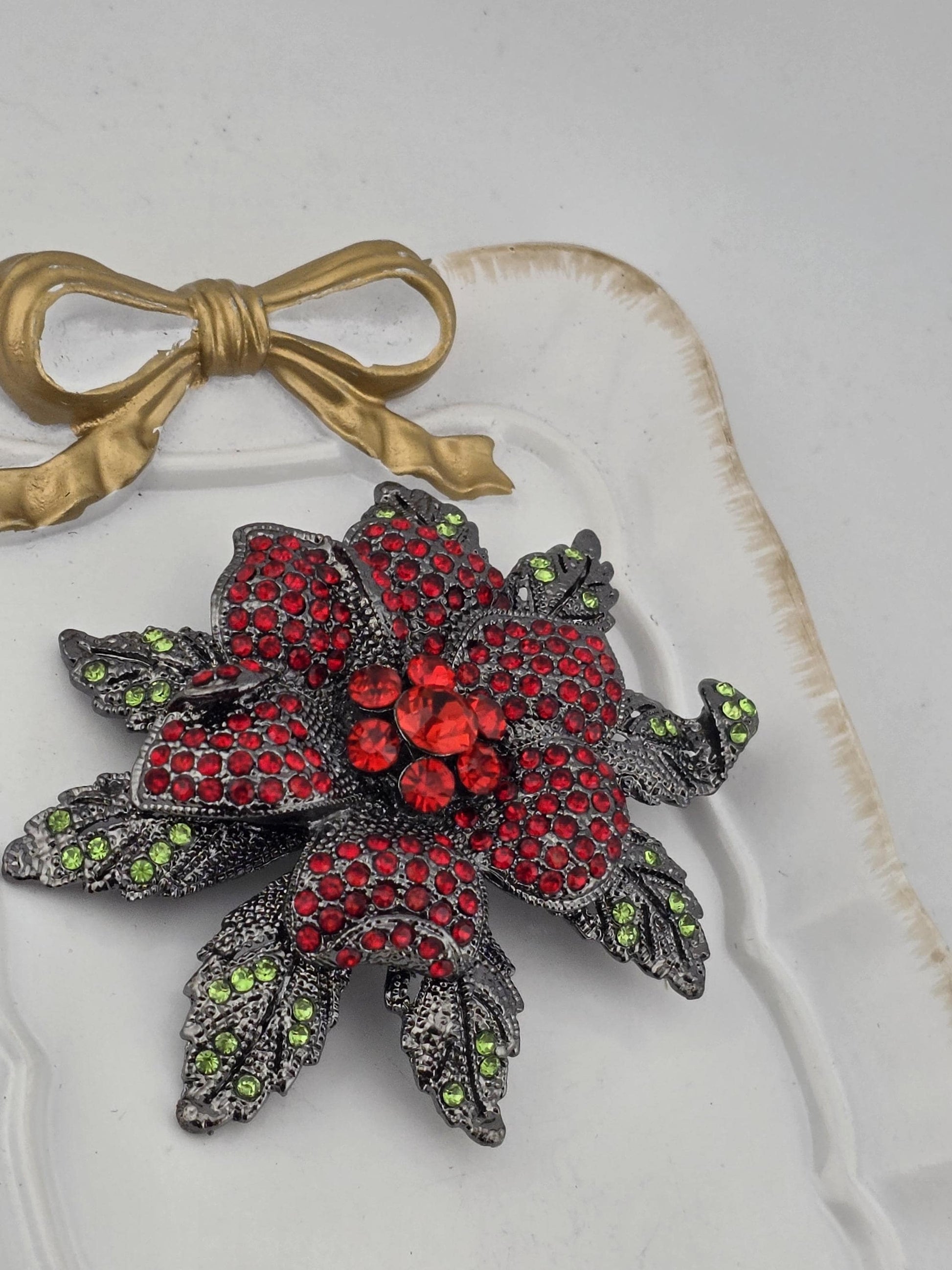 A decorative piece with a large red flower-shaped ornament and green leaves, adorned with sparkling gemstones.