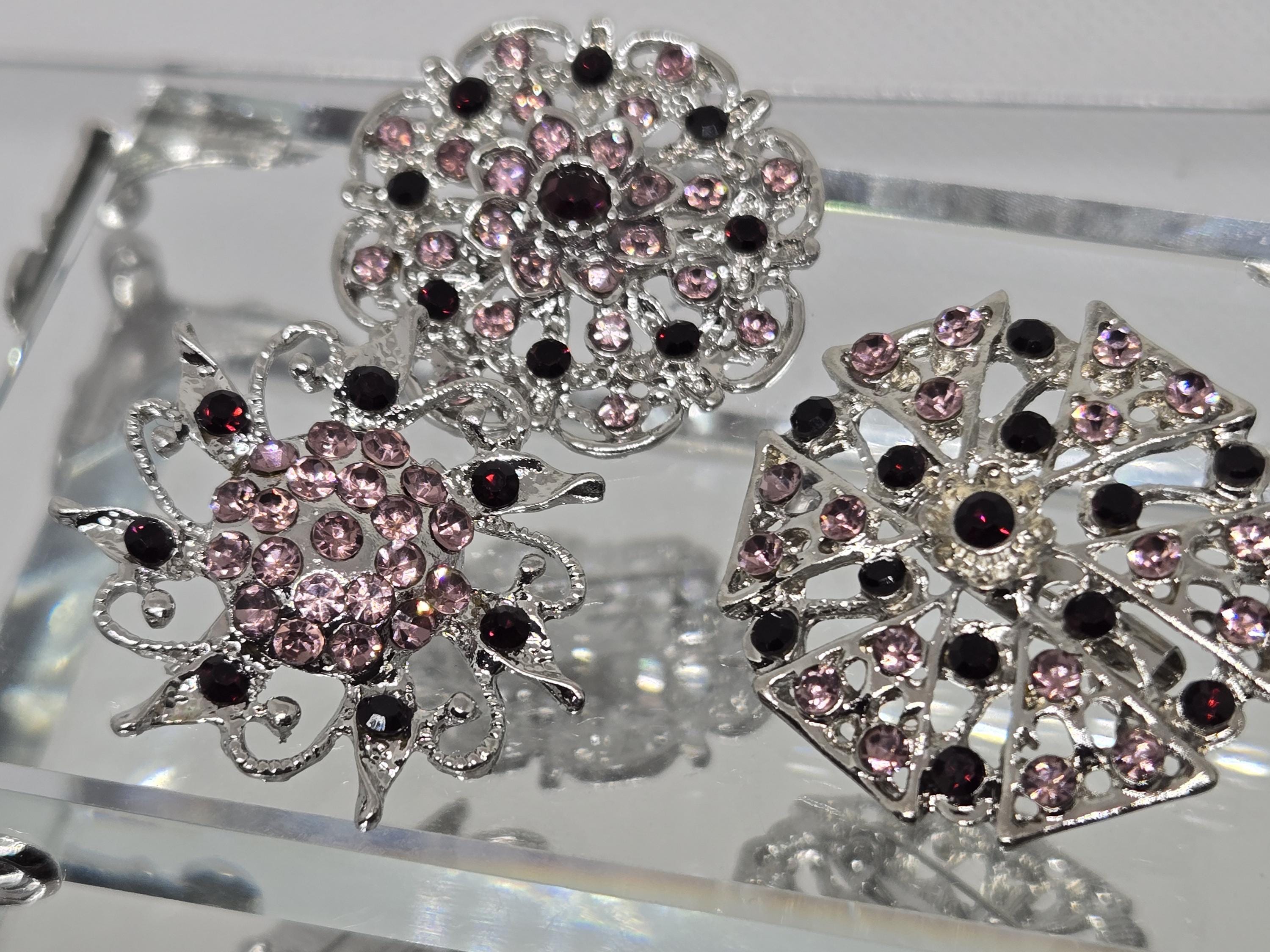 three ornate brooches with intricate designs and sparkling gemstones, including purple and black stones.