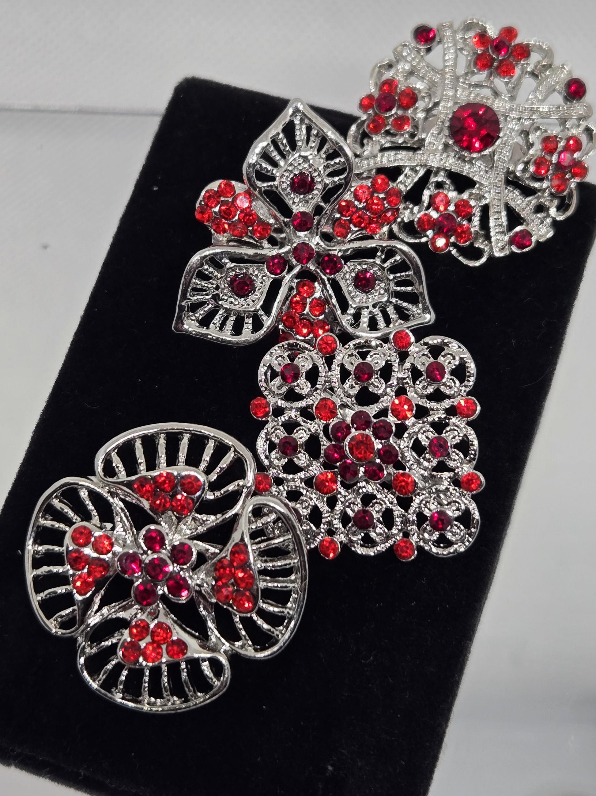a collection of ornate brooches adorned with red gemstones, displayed on a black velvet background.