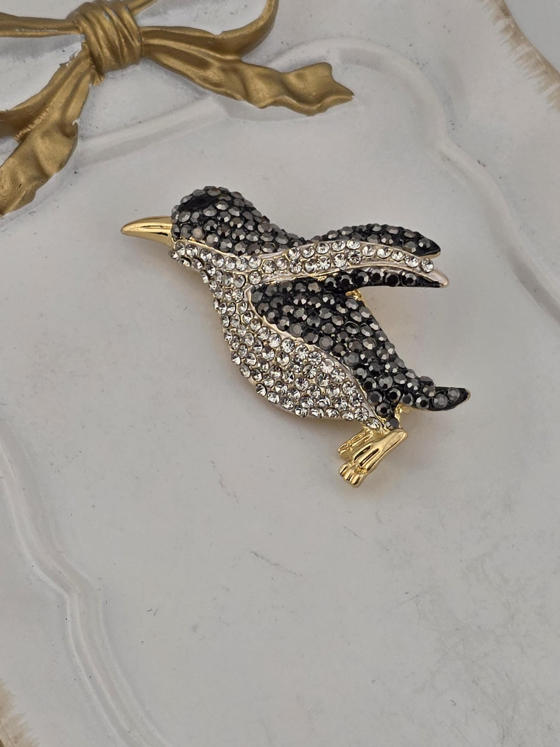 A decorative white frame with a black background, containing a sparkling rhinestone brooch in the shape of a bird.