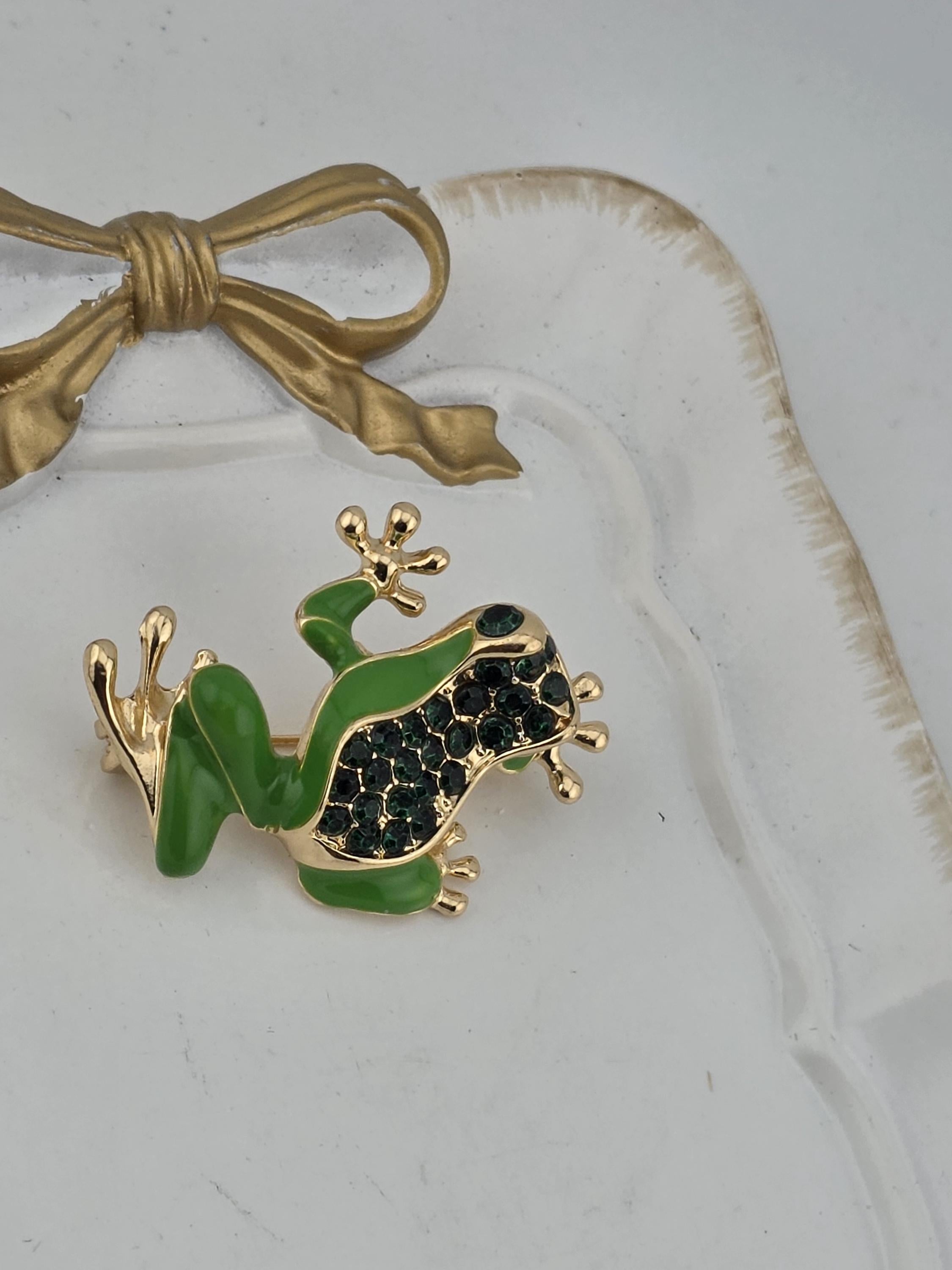 A decorative frog brooch with green and gold accents, featuring a large gemstone on its back.