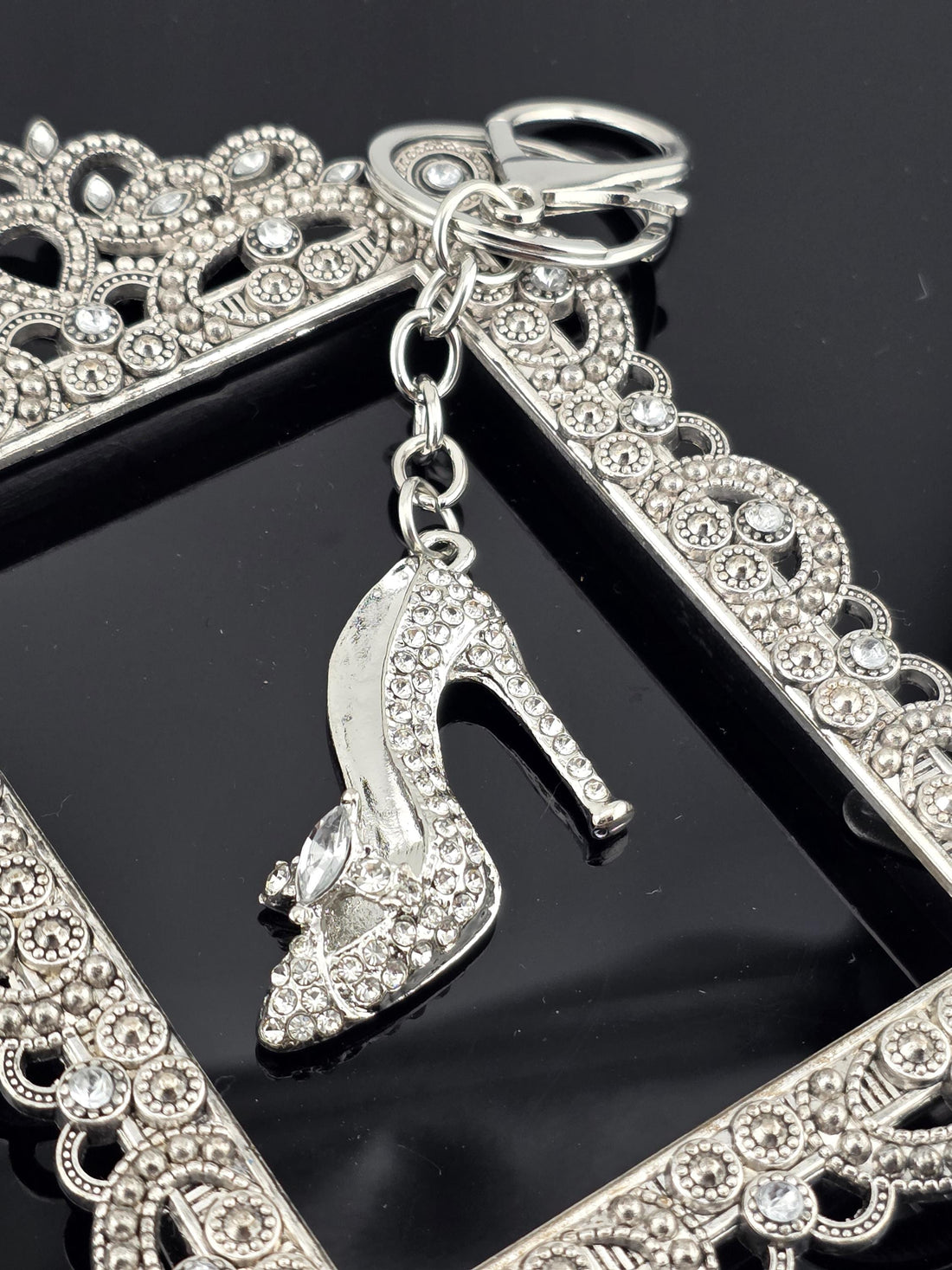 A close-up view of a silver-colored high heel shoe with rhinestones, attached to a decorative frame with a scalloped edge.