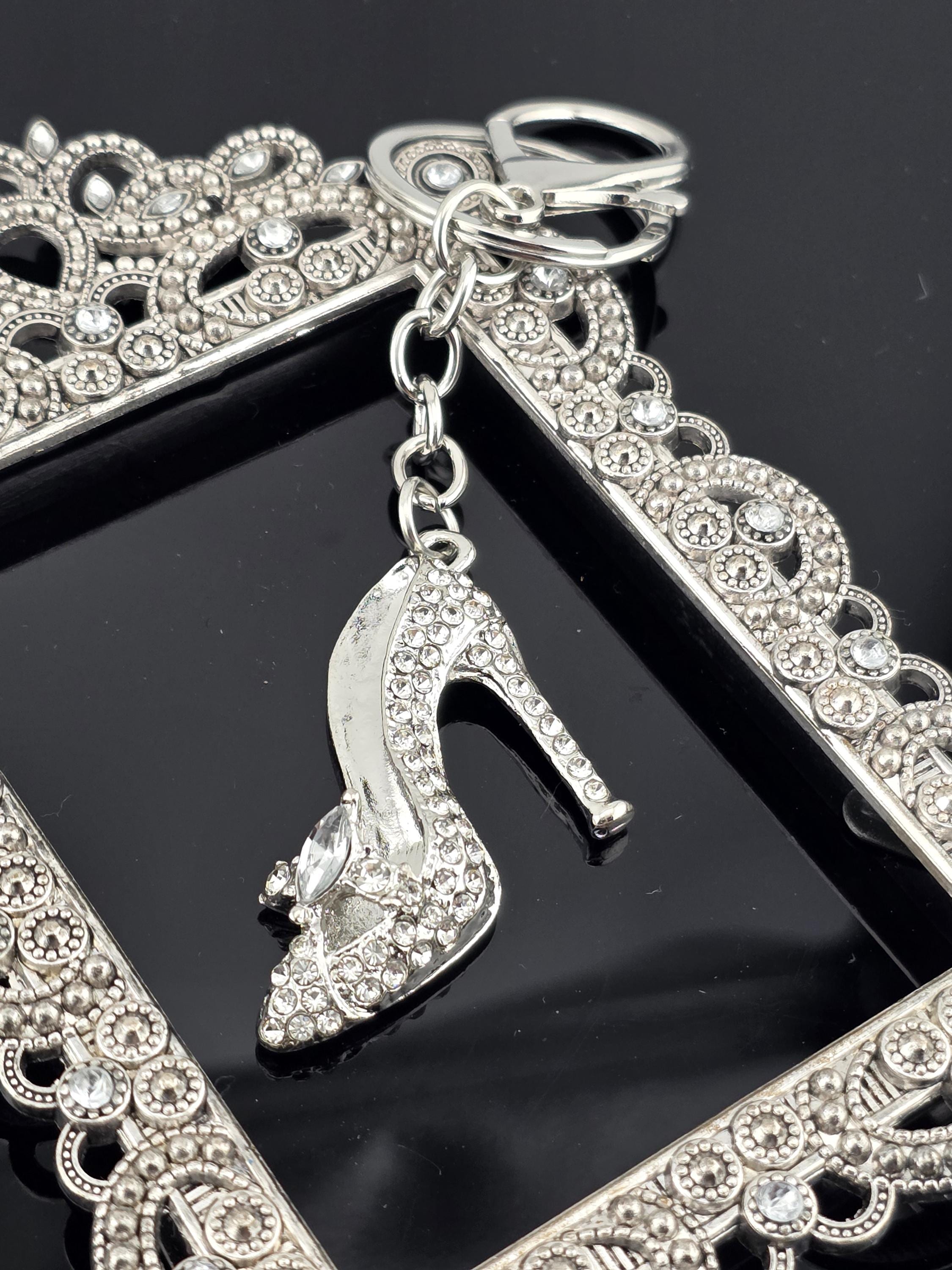 A close-up view of a silver-colored high heel shoe with rhinestones, attached to a decorative frame with a scalloped edge.