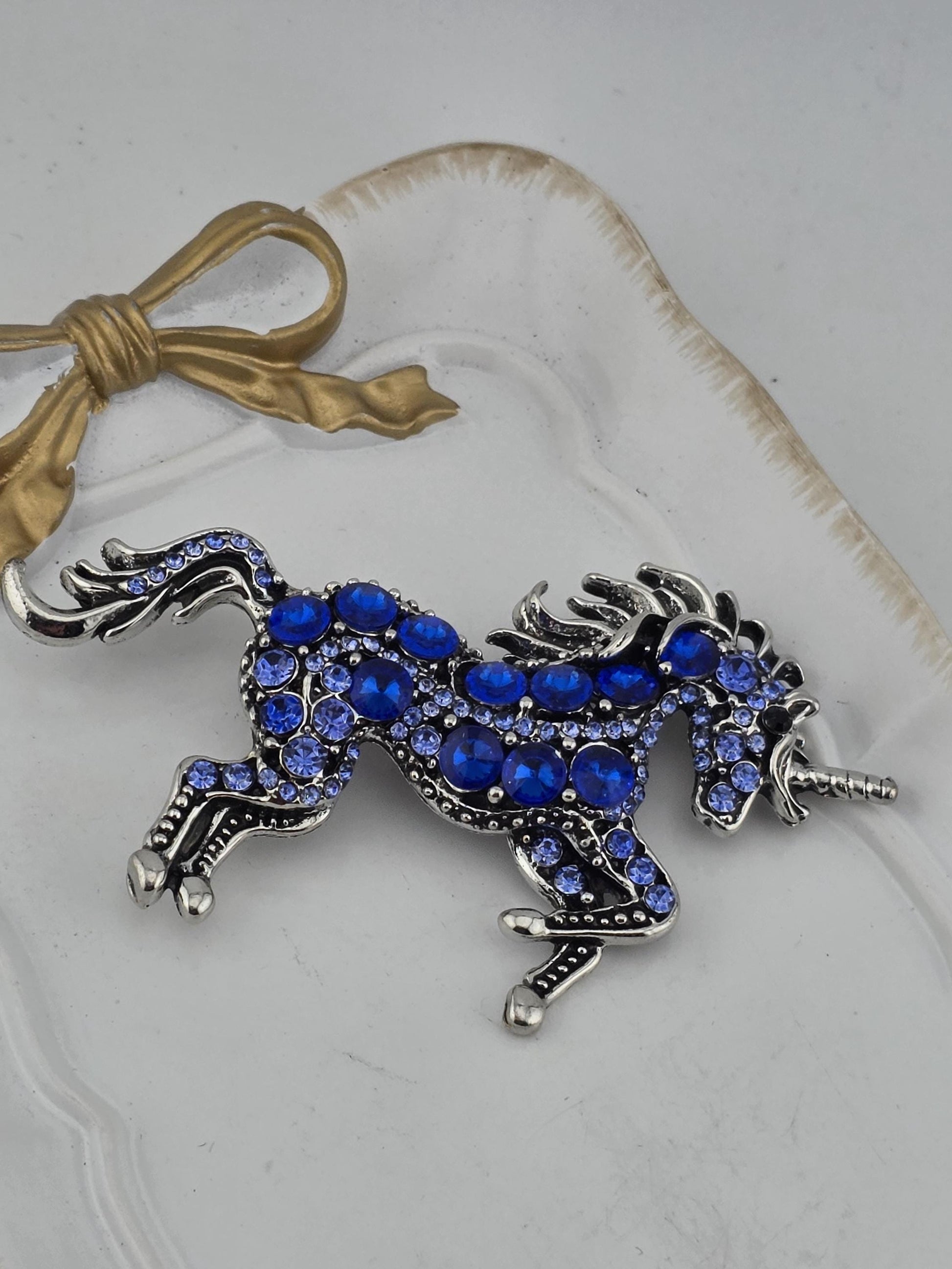 A decorative pendant in the shape of a unicorn, adorned with blue gemstones, is displayed on a white surface.