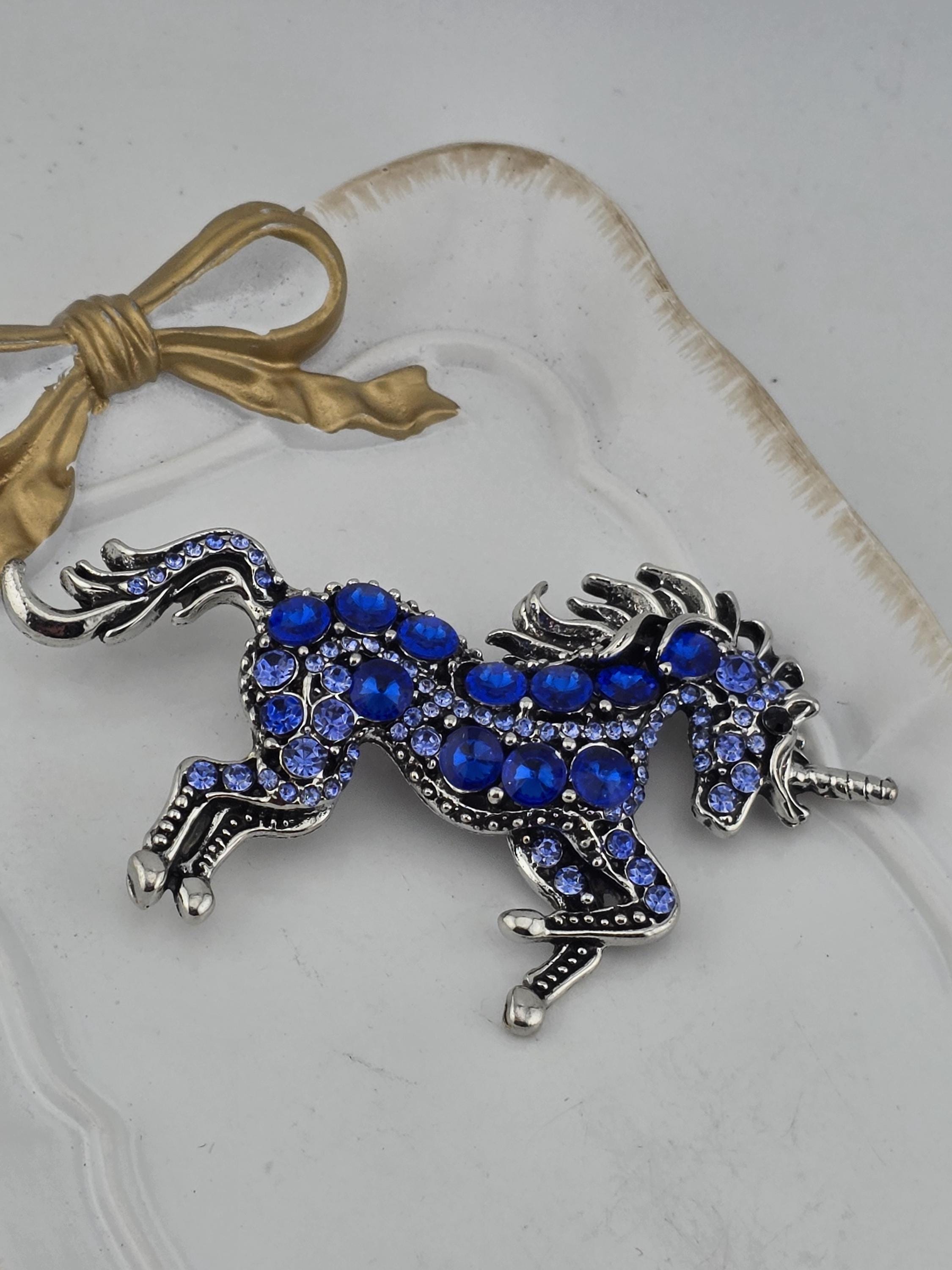 A decorative pendant in the shape of a unicorn, adorned with blue gemstones, is displayed on a white surface.