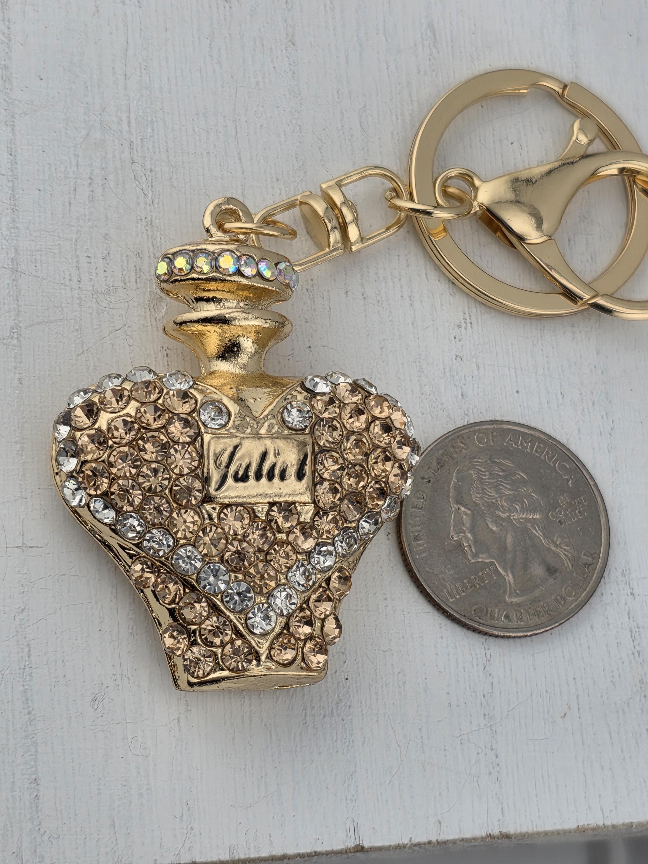 A decorative gold-colored perfume bottle keychain with rhinestones and a small coin placed next to it on a white surface.