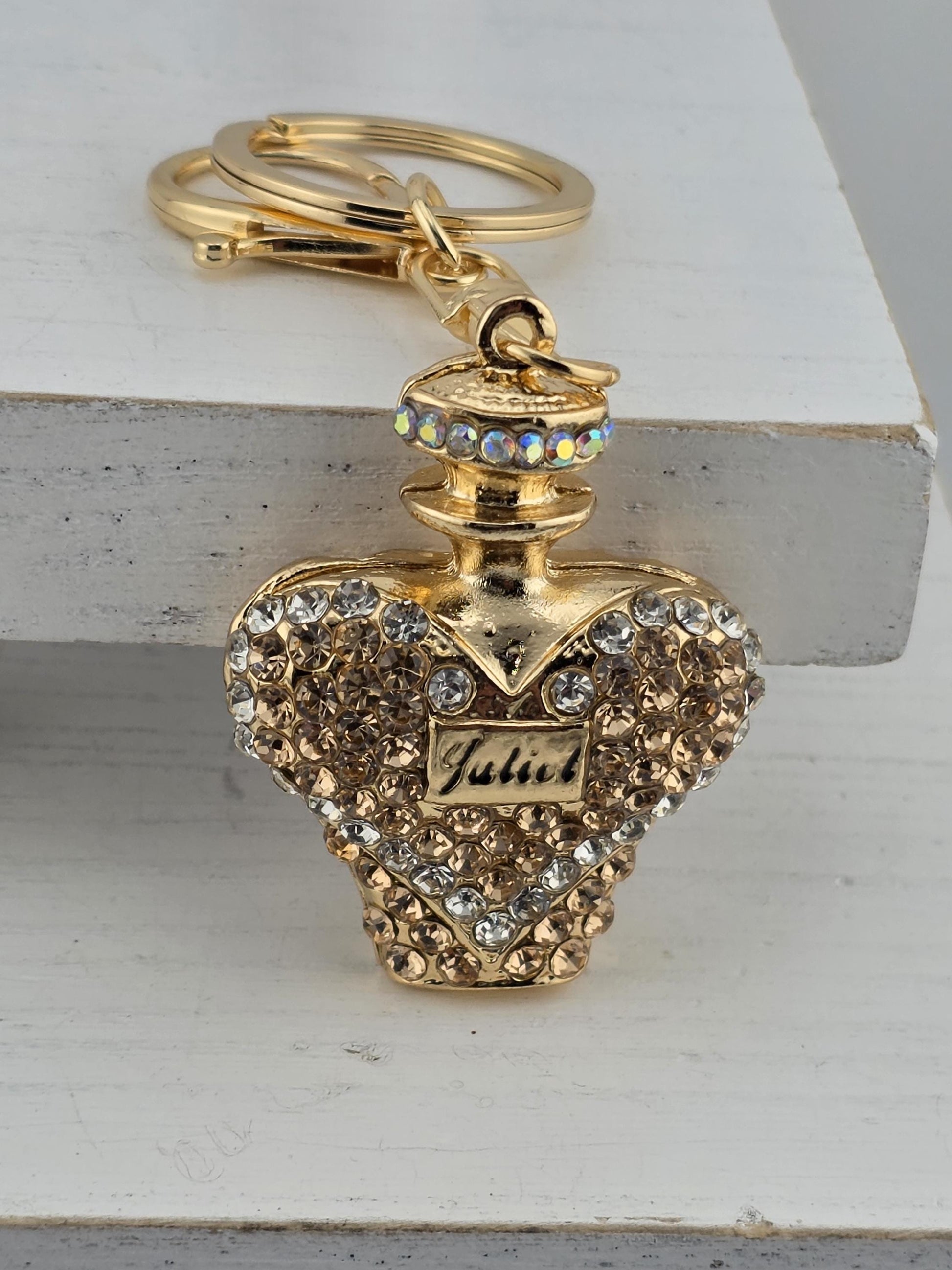 A decorative keychain with a gold-colored pendant adorned with rhinestones and a small label.