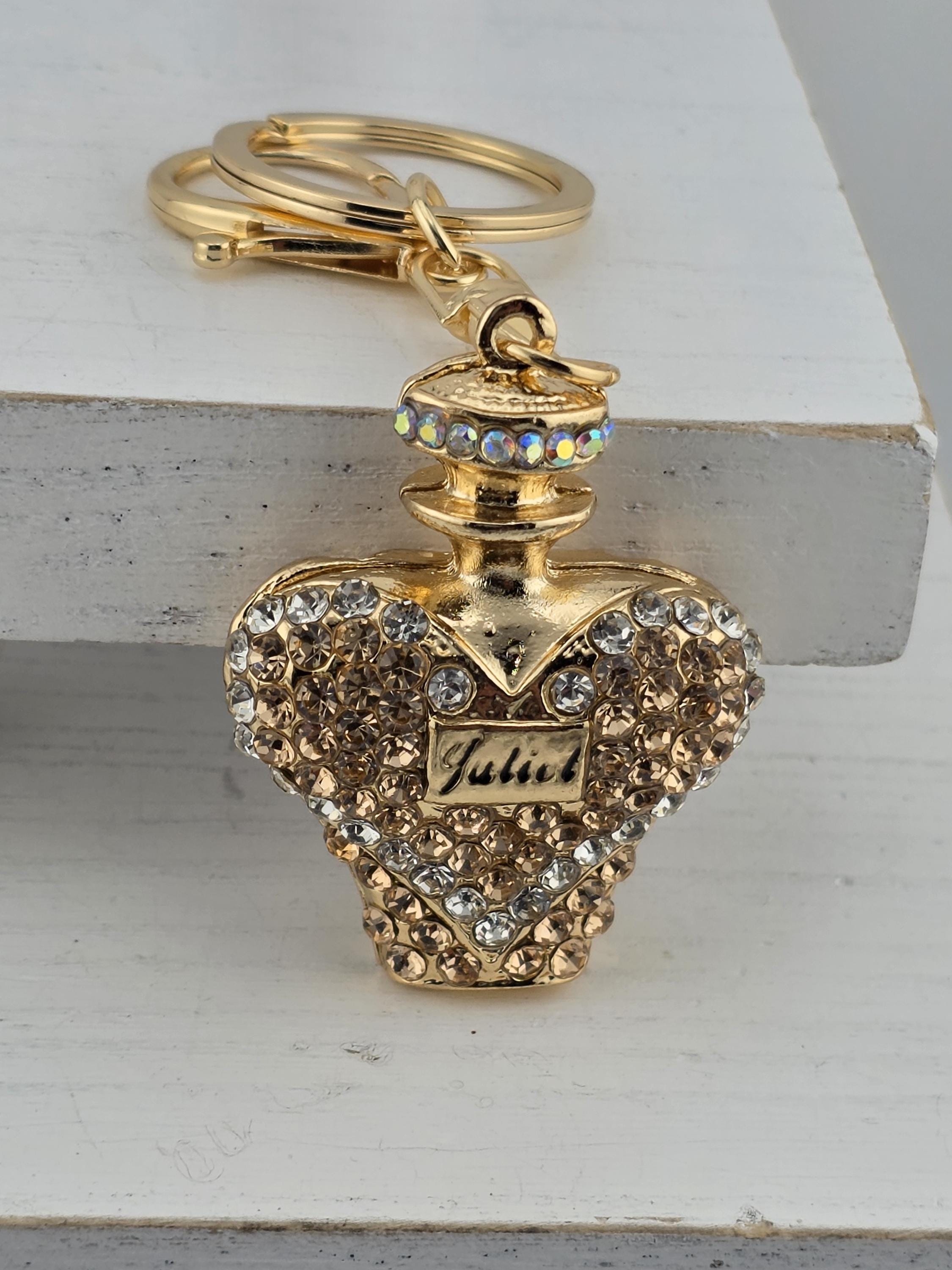 A decorative keychain with a gold-colored pendant adorned with rhinestones and a small label.