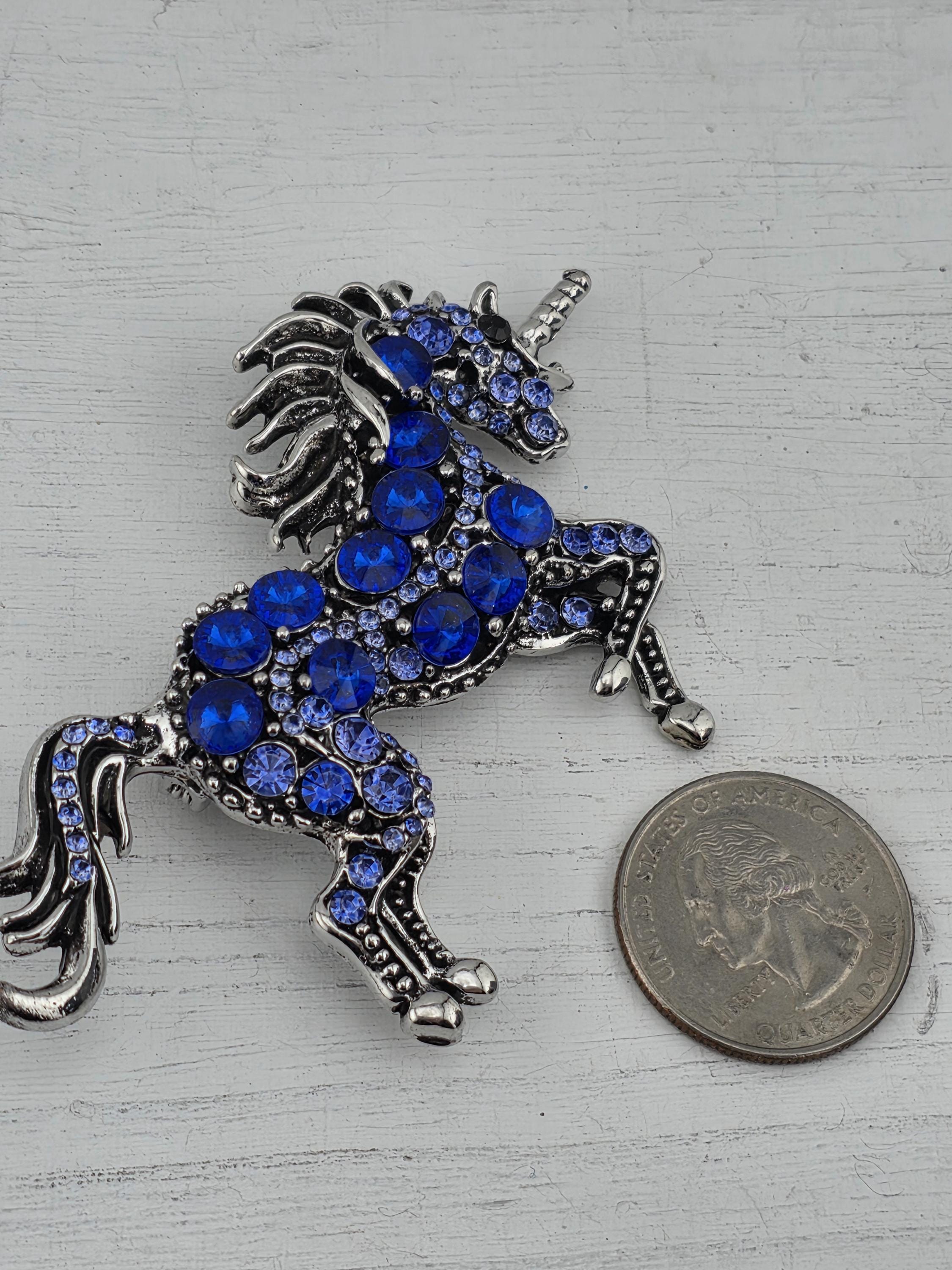 A silver brooch in the shape of a unicorn adorned with blue gemstones, placed next to a United States quarter.