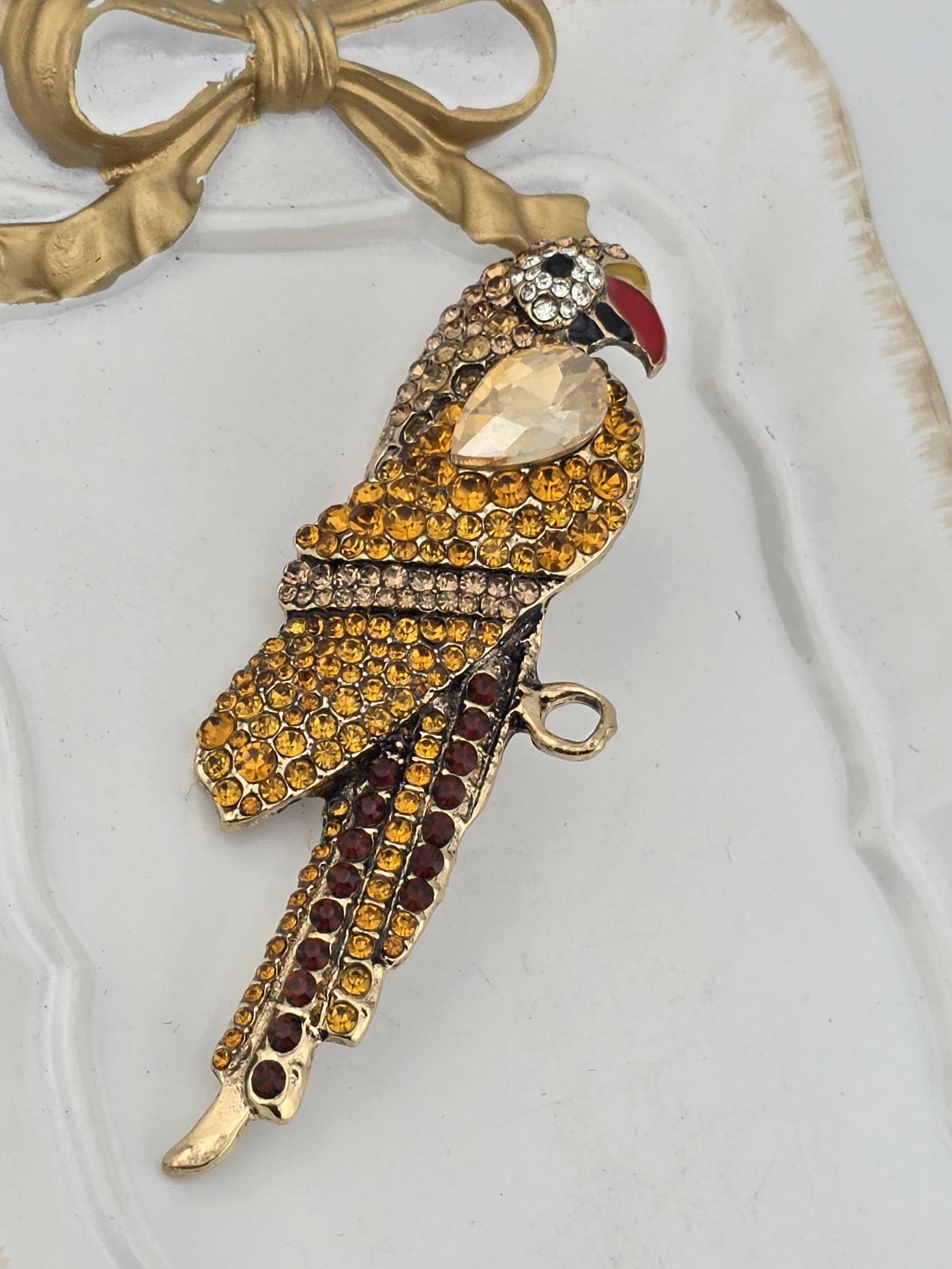 A decorative bird brooch with a gold and yellow color scheme, adorned with numerous small gemstones.