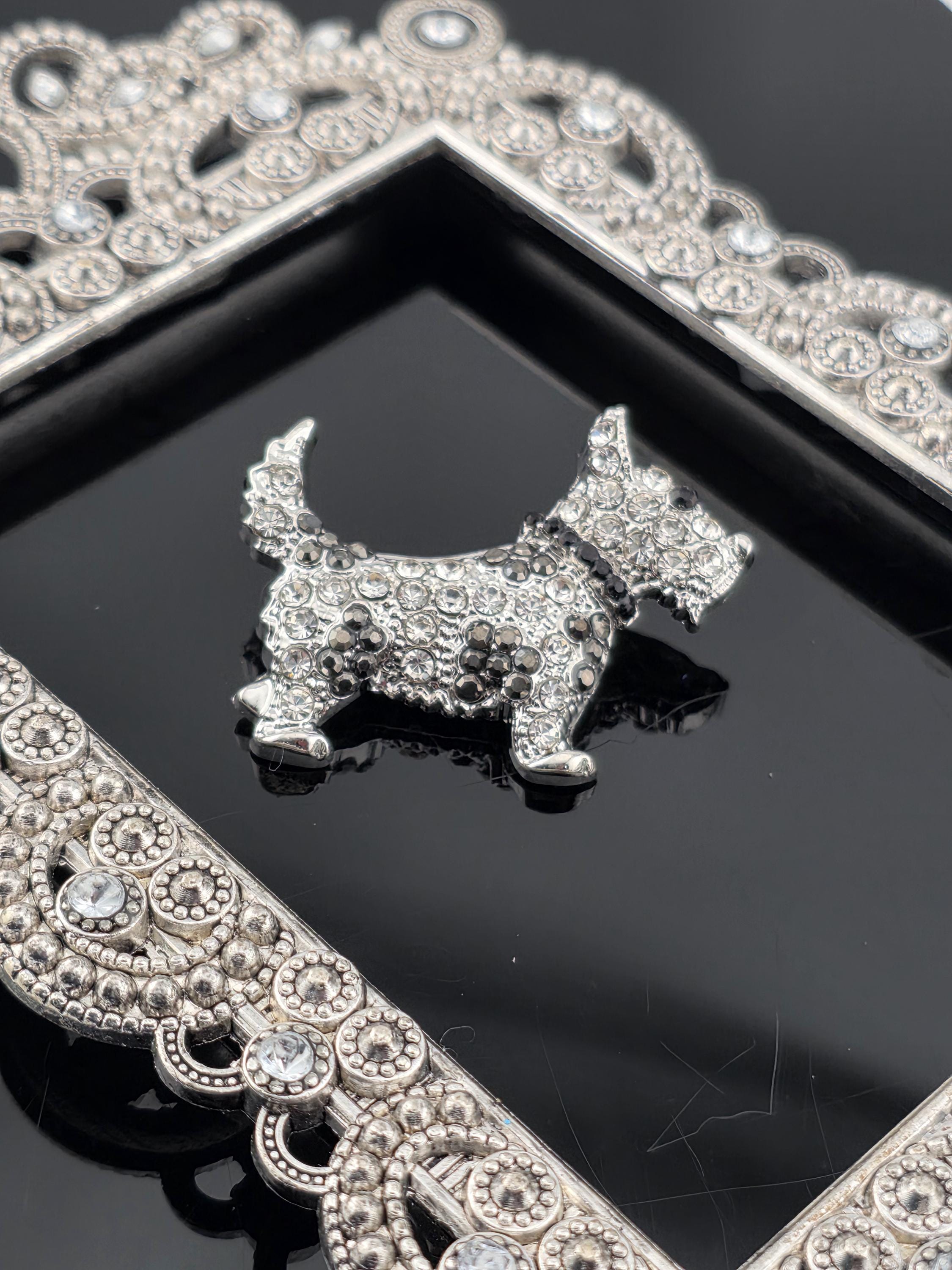 A close-up of a silver-colored ornate frame with a small, intricately-designed dog-shaped brooch or pendant.