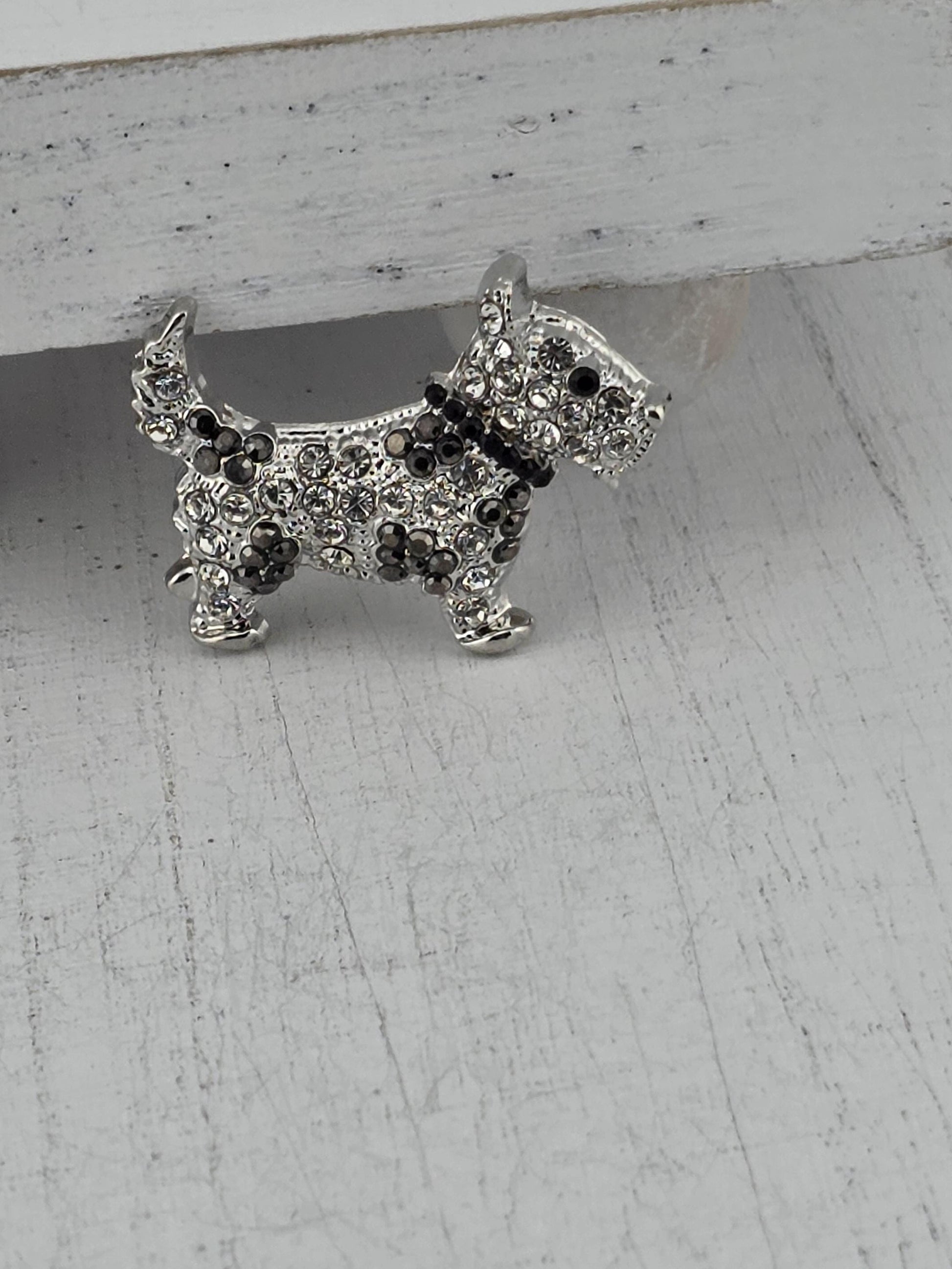 A silver-colored decorative dog brooch with a sparkling crystal design.