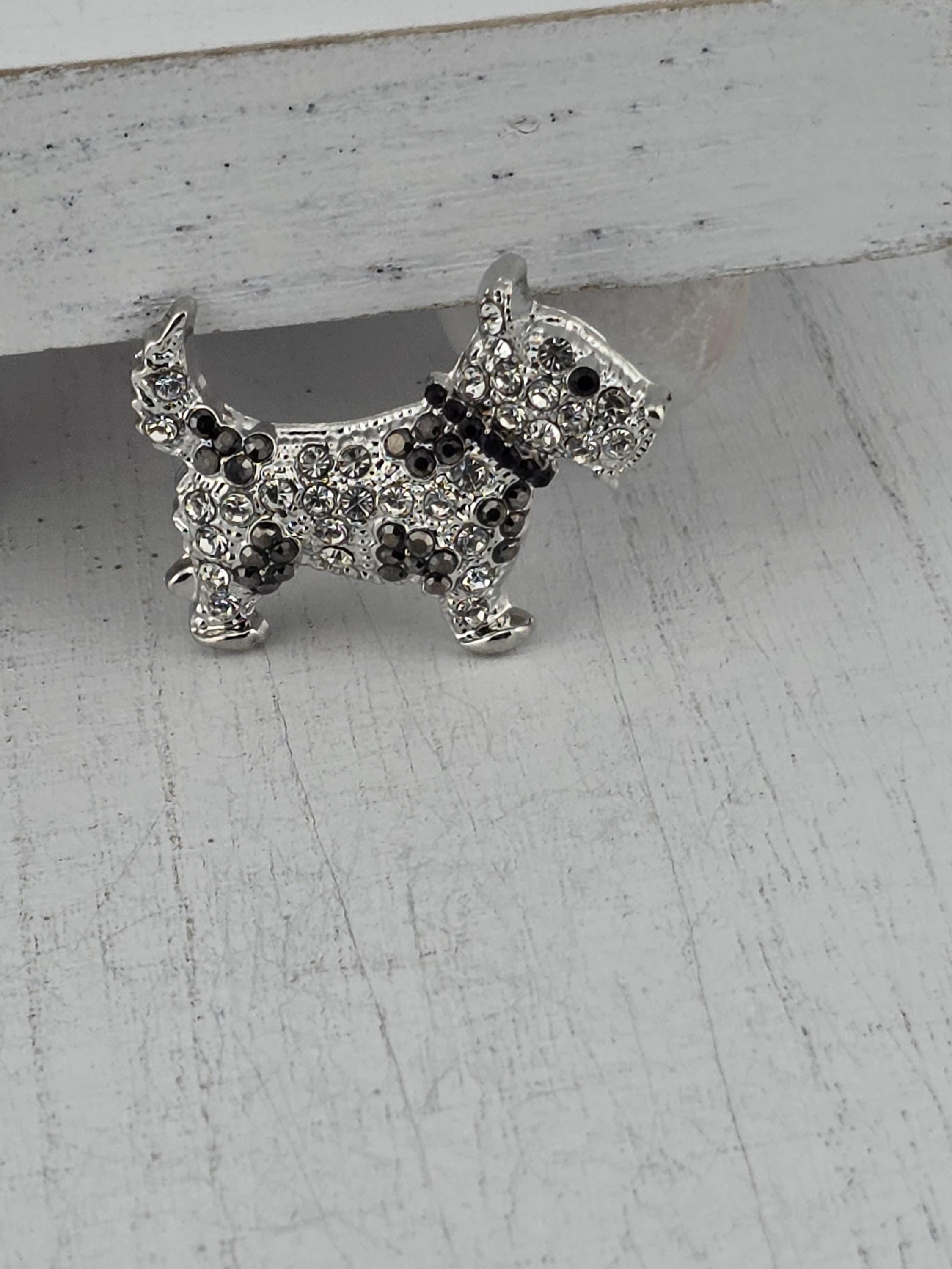 A silver-colored decorative dog brooch with a sparkling crystal design.