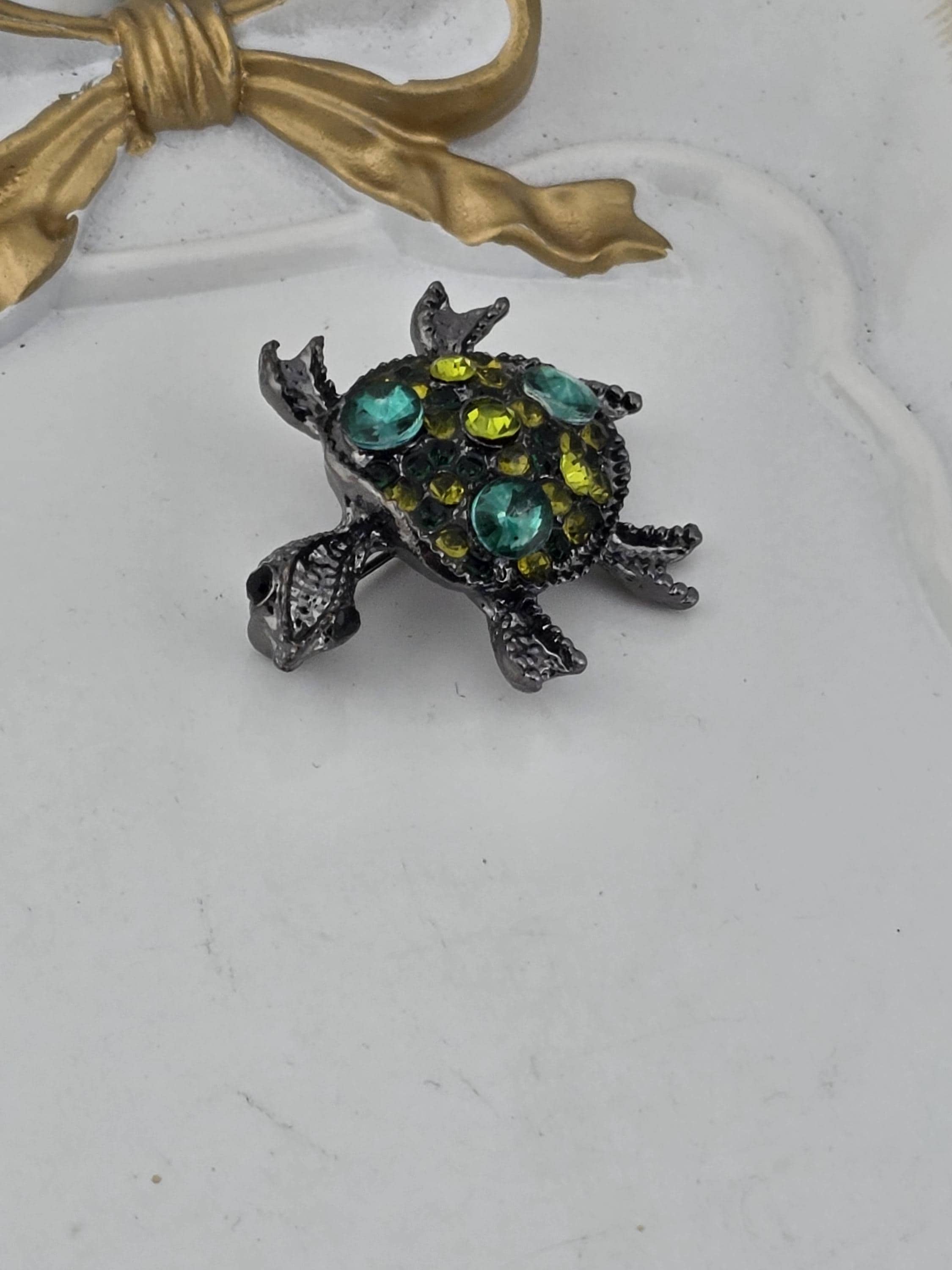 A decorative turtle-shaped brooch with colorful gemstones is displayed on a white surface.