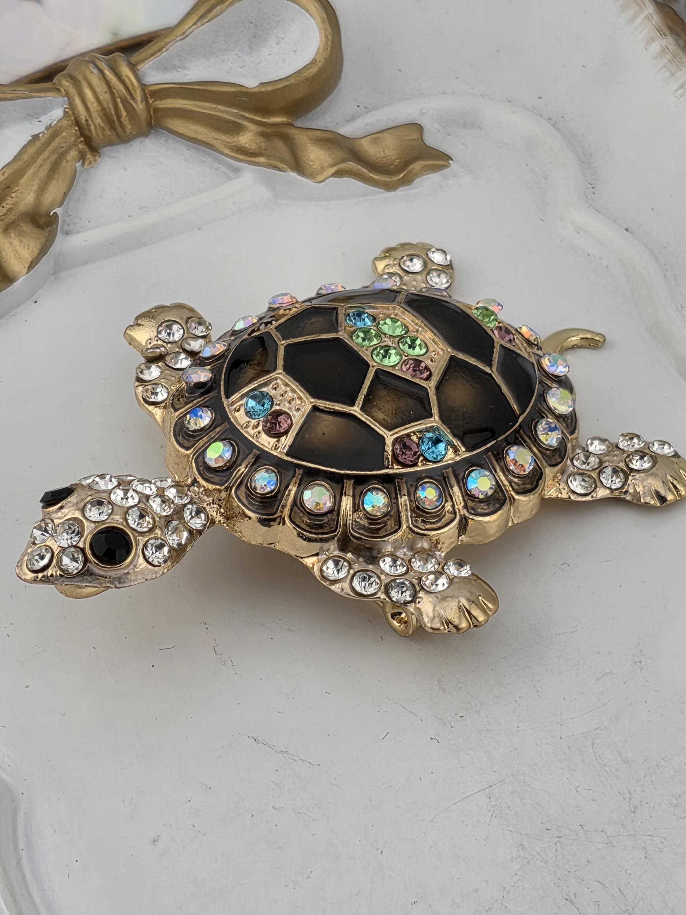 A decorative turtle brooch with a black shell and gold-colored body, adorned with colorful gemstones and rhinestones.