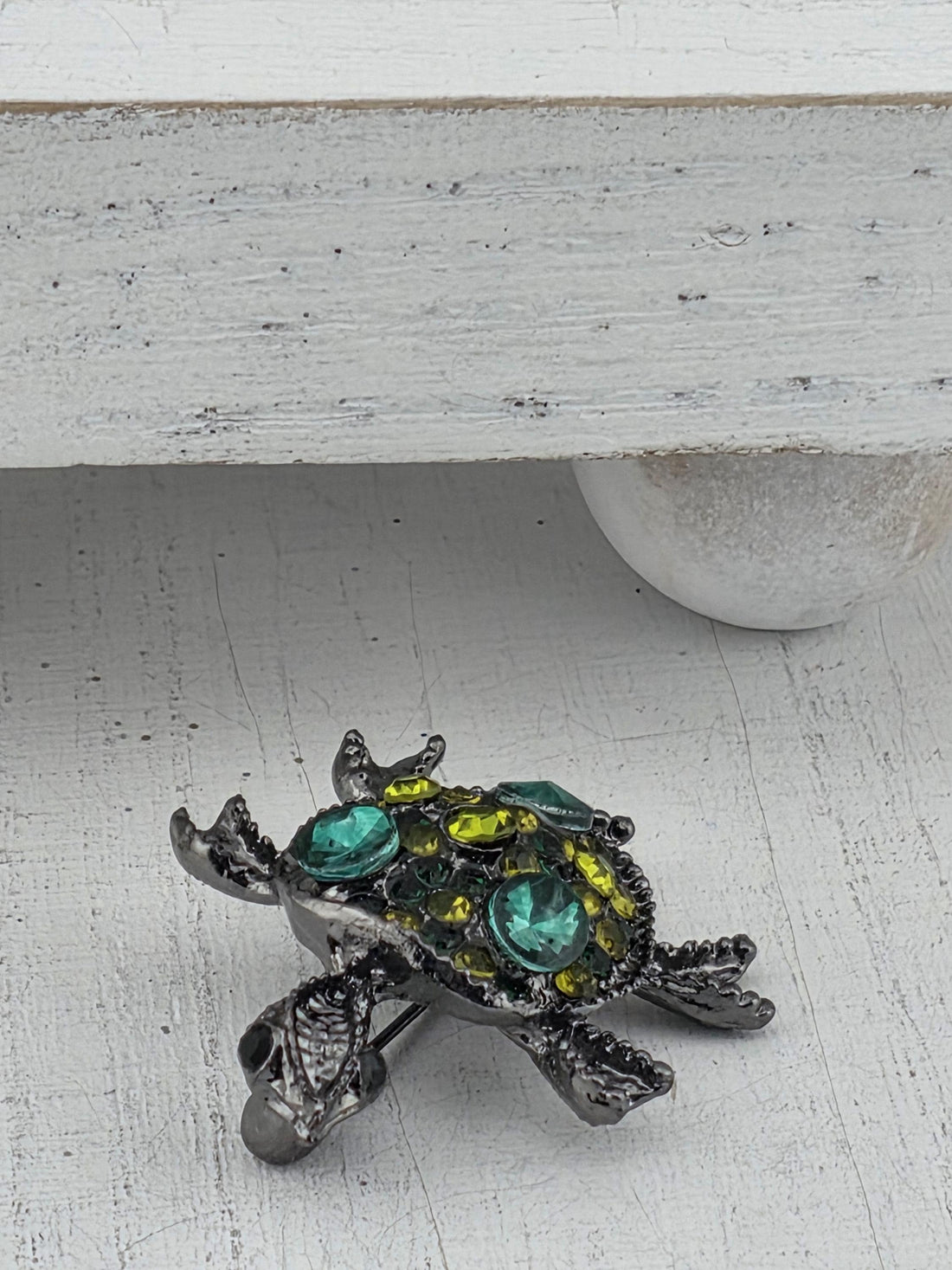 A decorative turtle-shaped brooch with colorful gemstones is displayed on a white surface.