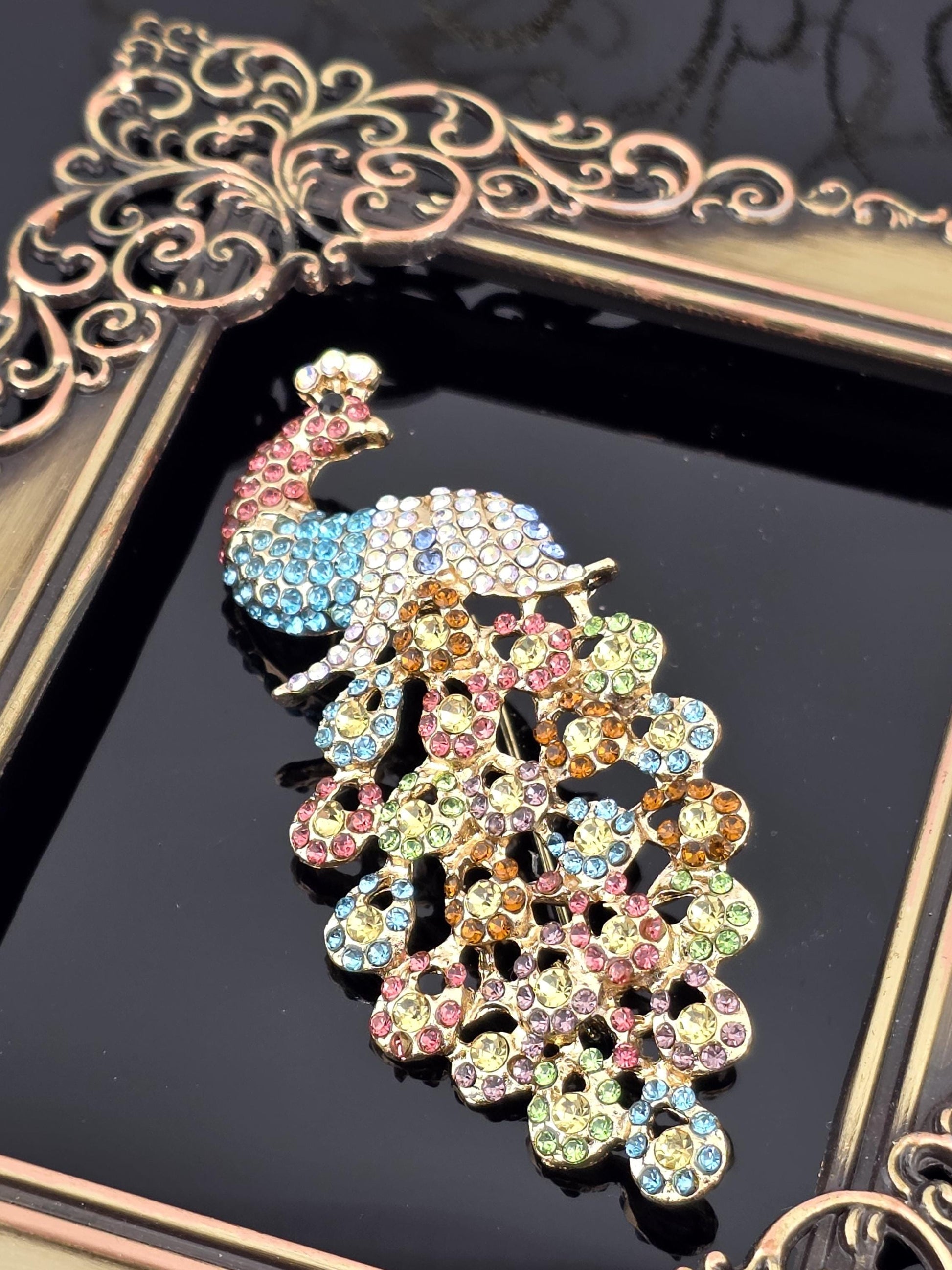 A decorative peacock brooch with colorful gemstones is displayed in a gold frame.