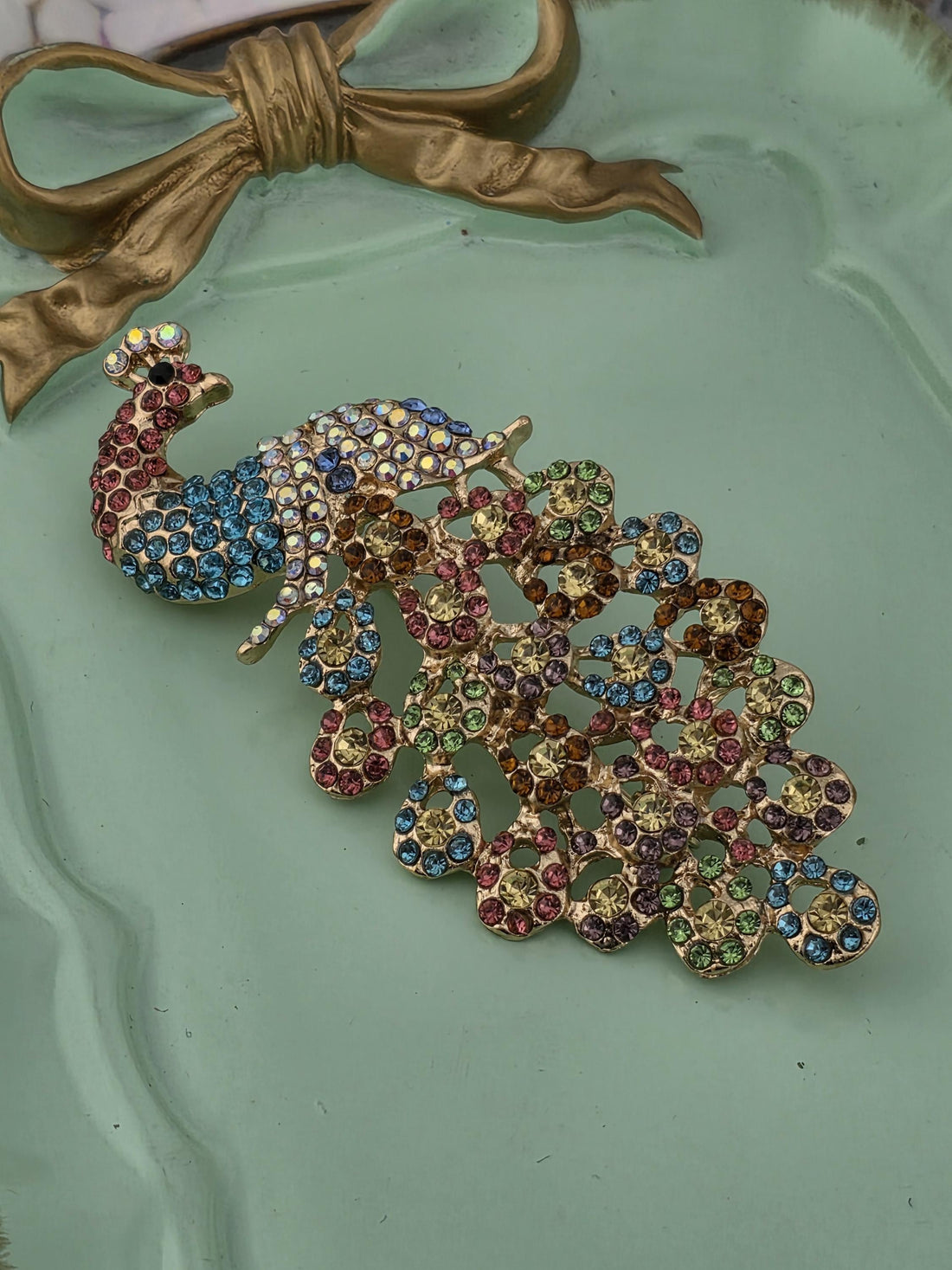 A decorative peacock brooch with colorful gemstones is displayed in a gold frame.