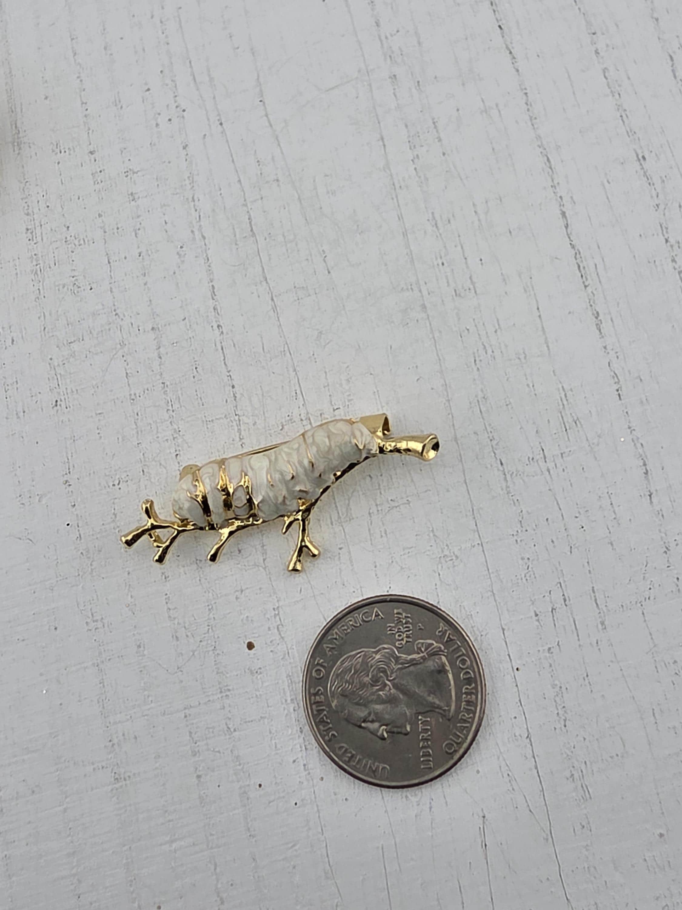 A gold-colored pendant in the shape of a fish is placed next to a United States quarter on a white wooden surface.