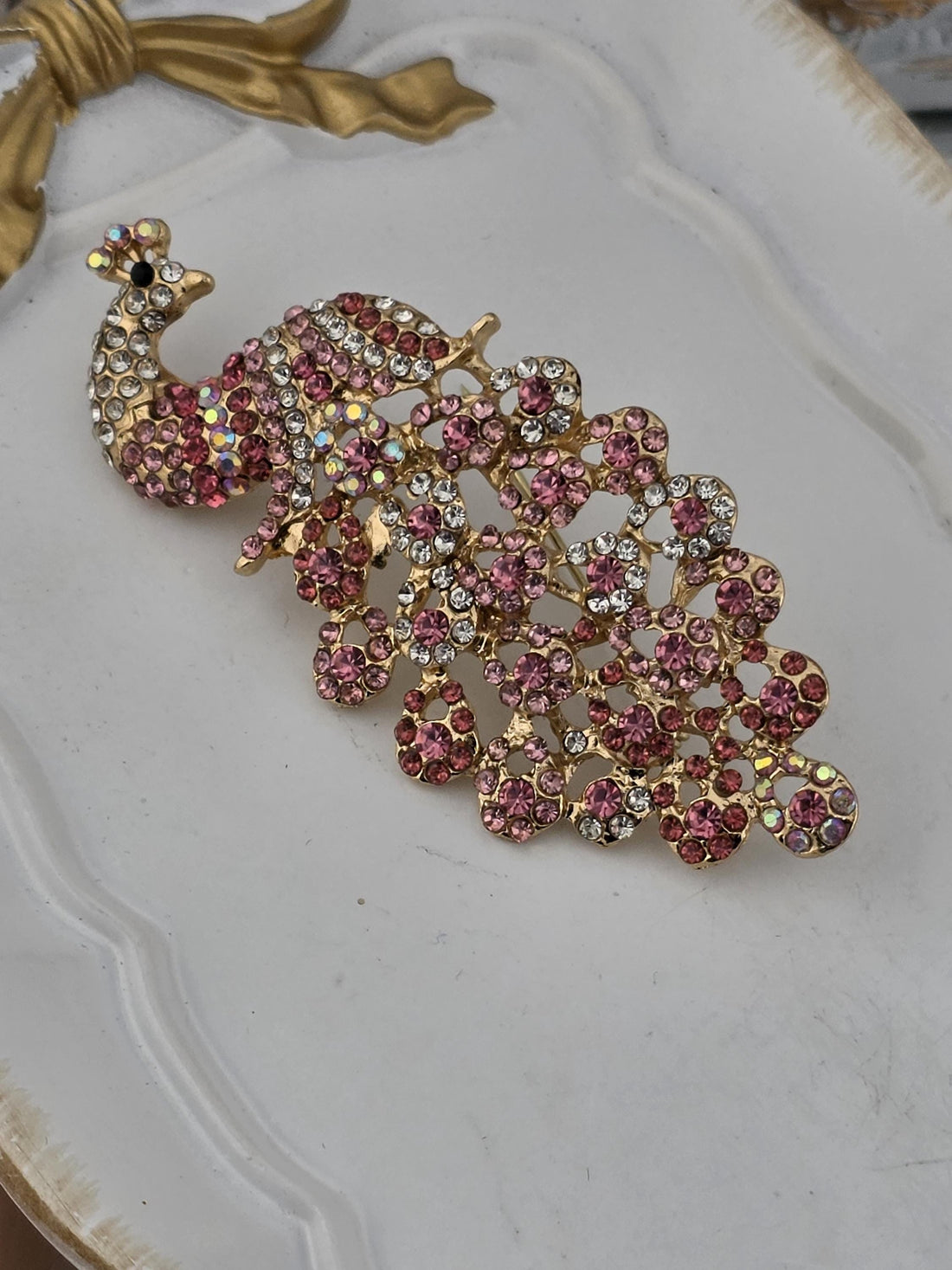 A decorative gold and black frame with a large, ornate peacock brooch with pink and white gemstones.