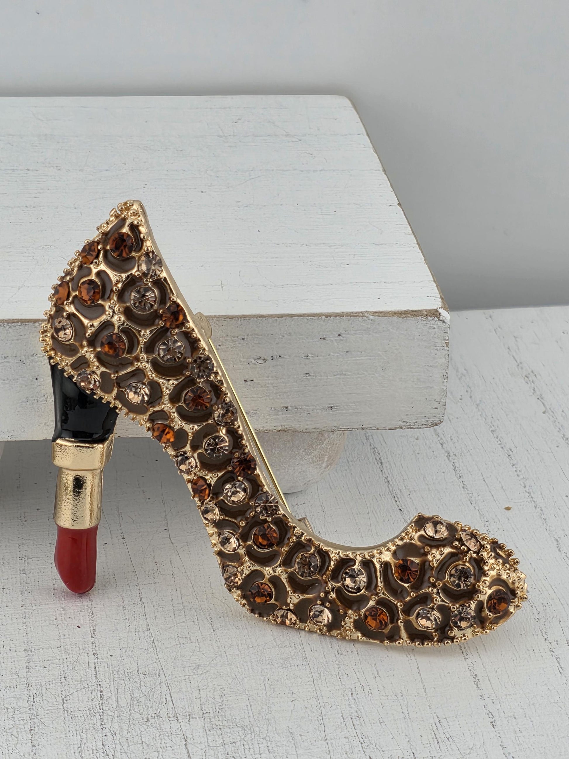A gold-colored, diamond-encrusted brooch is attached to a red lipstick, creating an elegant and eye-catching display.