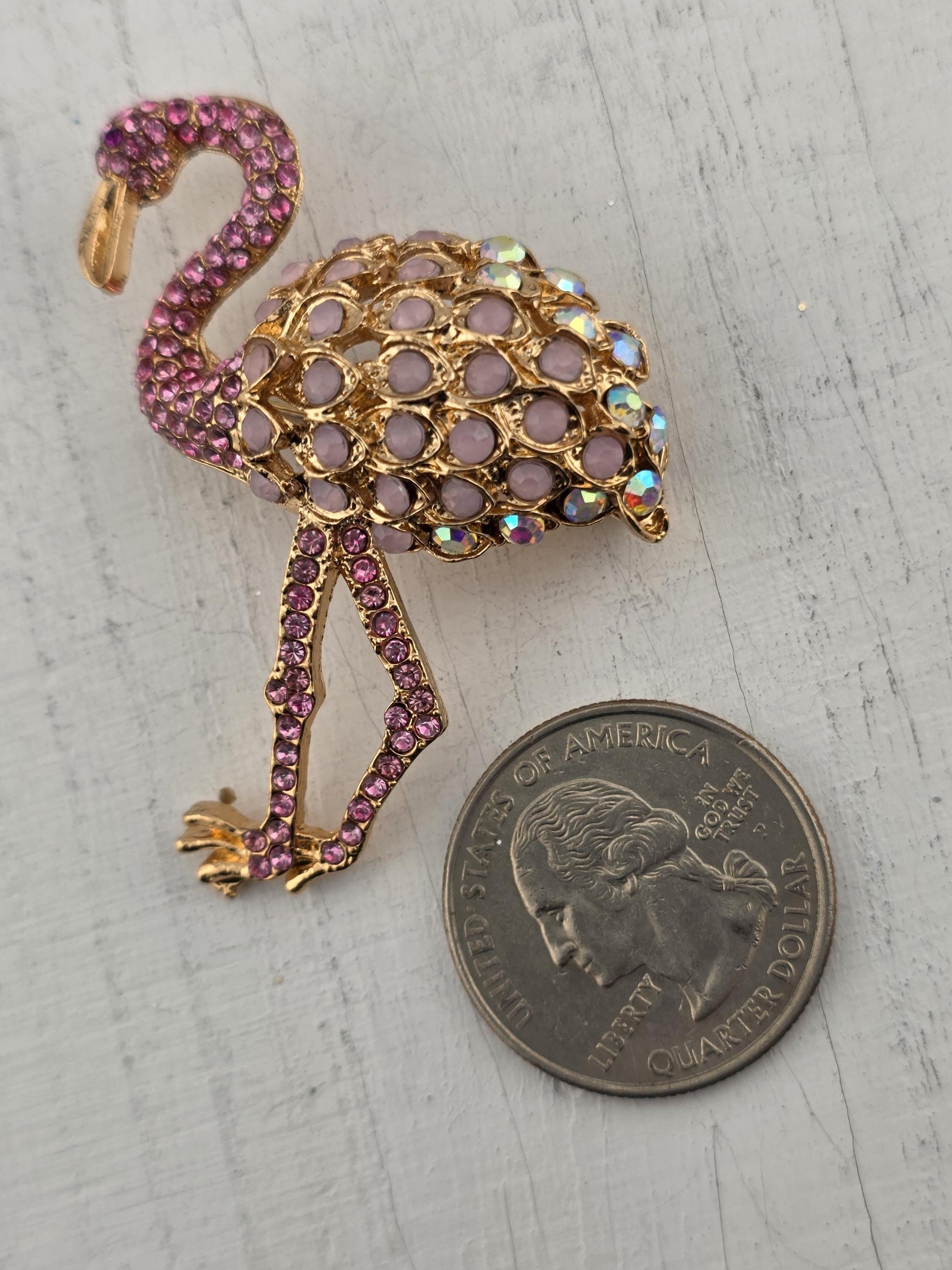 a decorative piece of jewelry, which appears to be a brooch or pendant, adorned with a combination of purple and gold gemstones. The piece is placed next to a United States quarter, indicating its value.