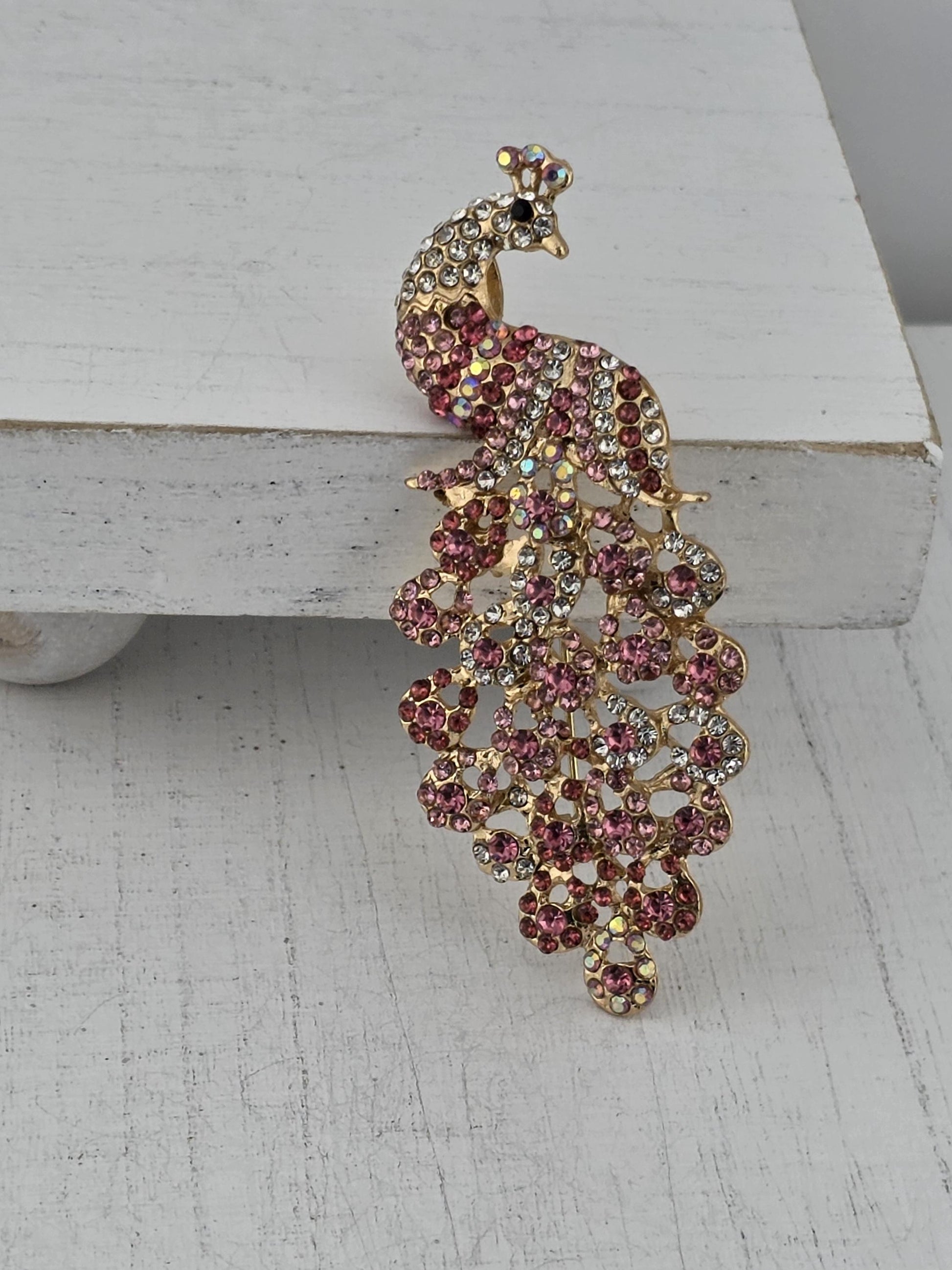 A decorative piece of jewelry featuring a peacock design, with a combination of pink and gold gemstones.
