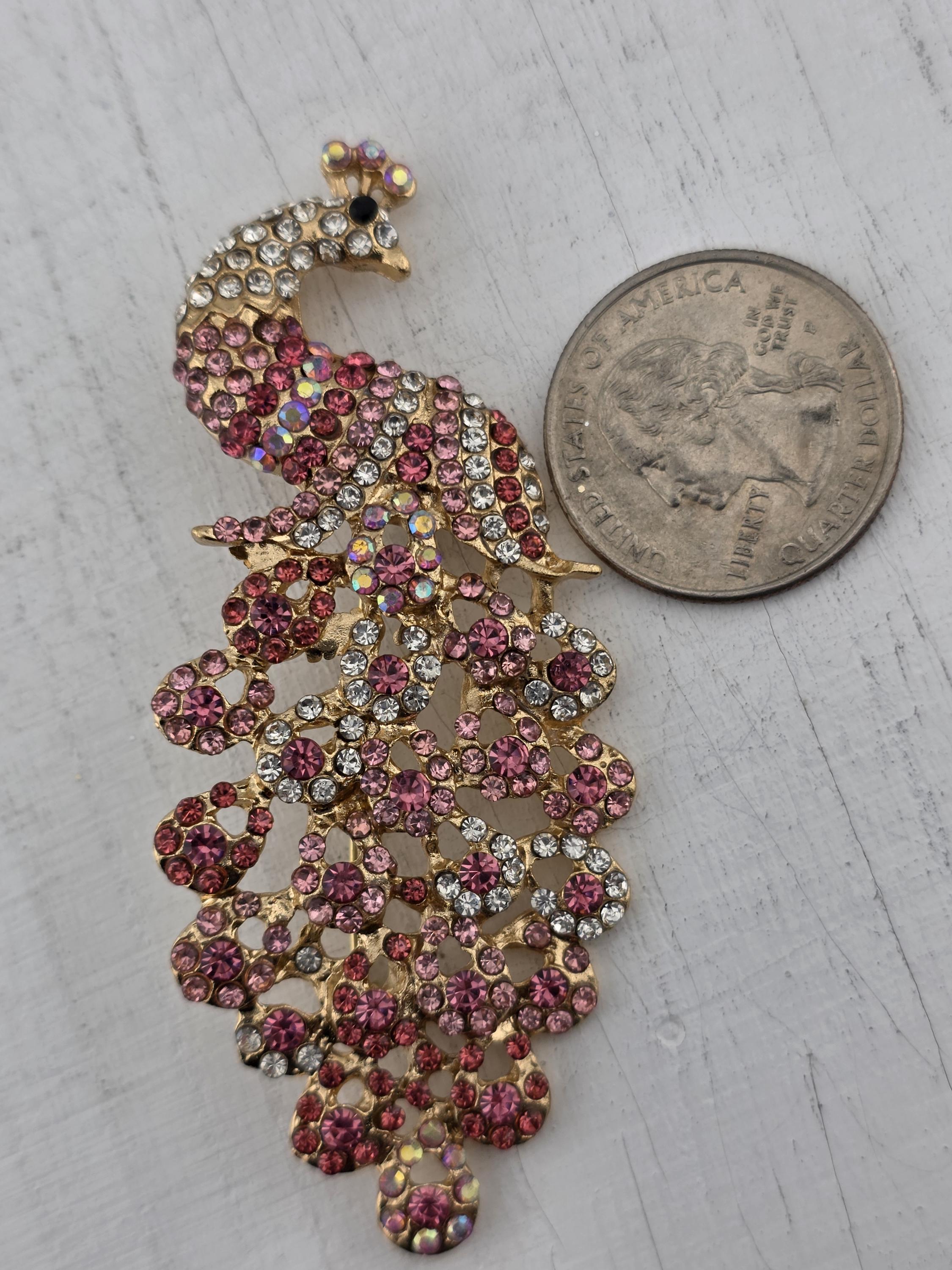 A close-up image of a decorative piece, possibly a brooch or necklace, with a large, shiny coin placed next to it on a white surface.