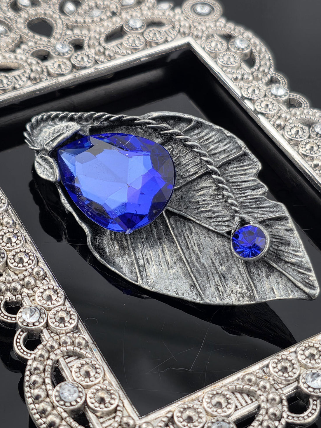 a close-up view of a decorative silver leaf-shaped frame with a large blue gemstone set in it.