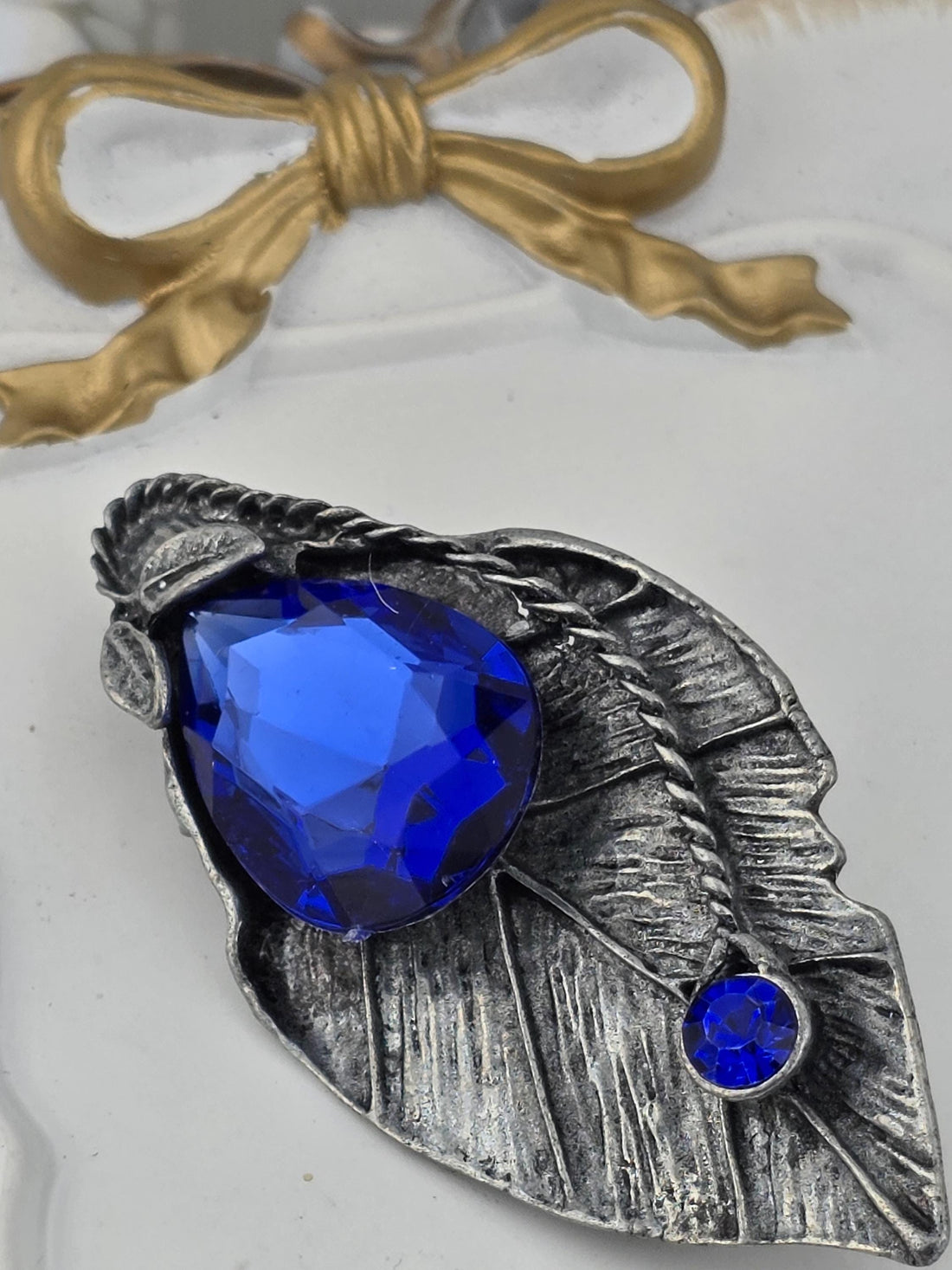 a close-up view of a decorative silver leaf-shaped frame with a large blue gemstone set in it.