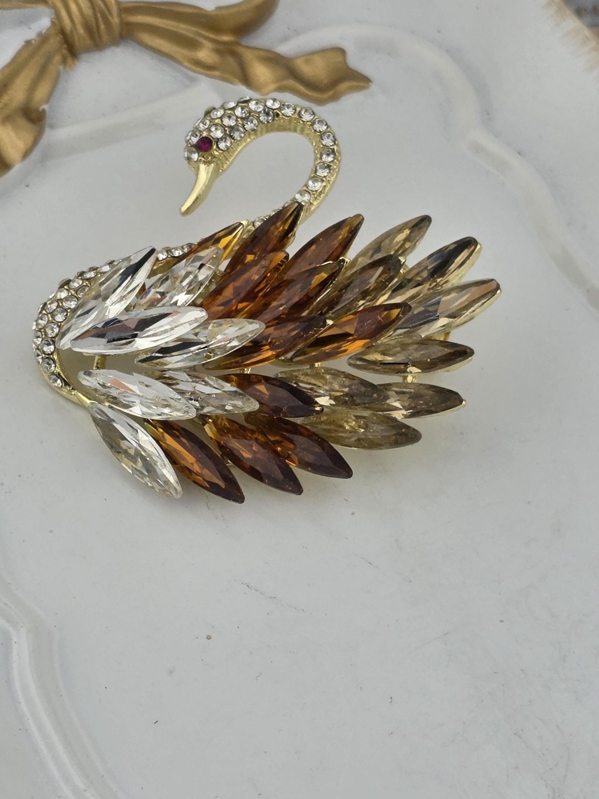 A decorative brooch with a swan-like design, featuring a combination of gold, brown, and clear gemstones.