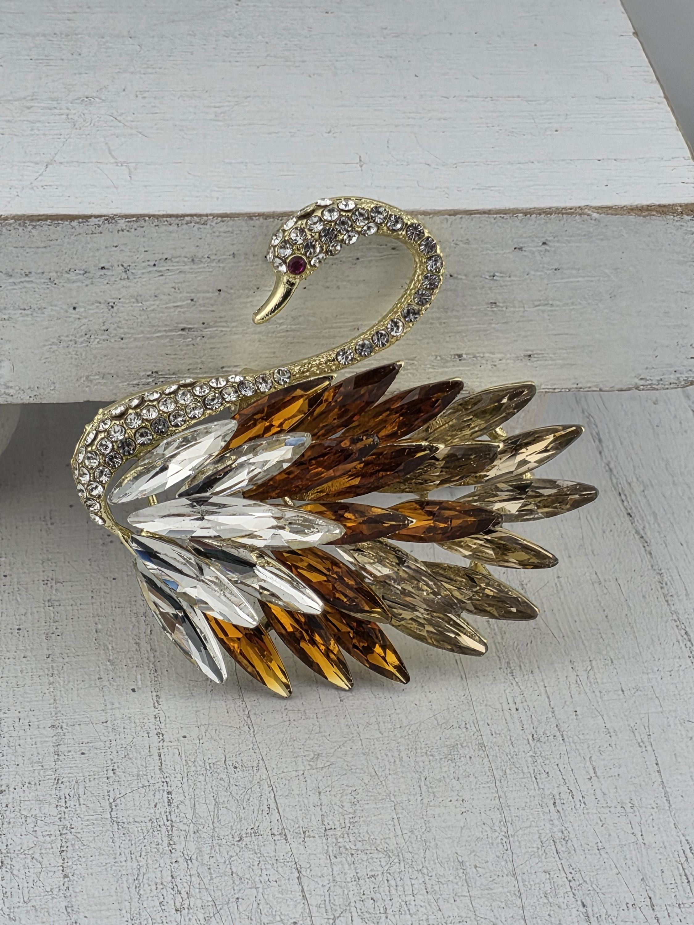 A decorative swan brooch with a gold and brown color scheme, adorned with numerous sparkling rhinestones.