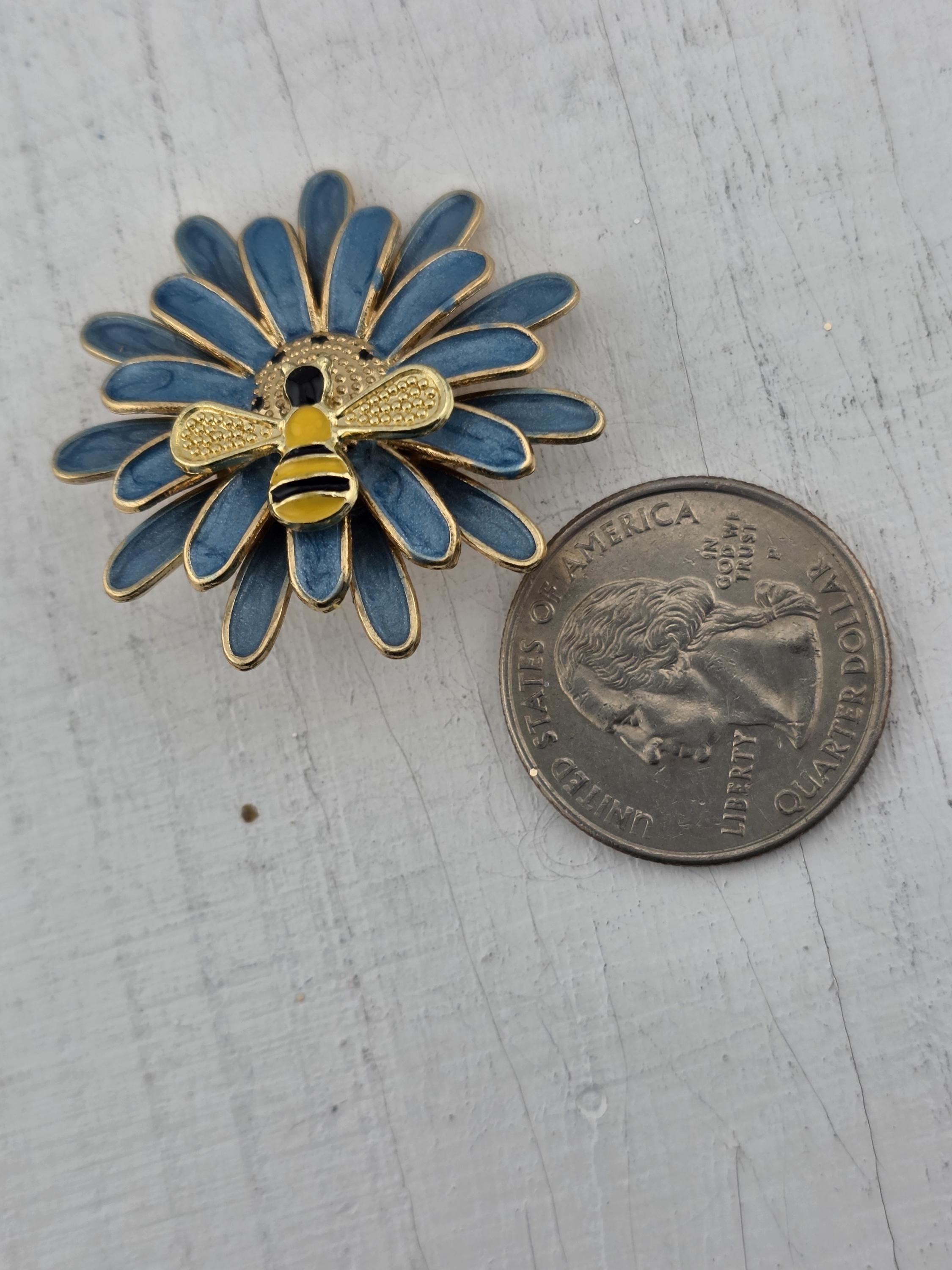 a blue and gold pin with a bee design, placed next to a United States quarter coin.