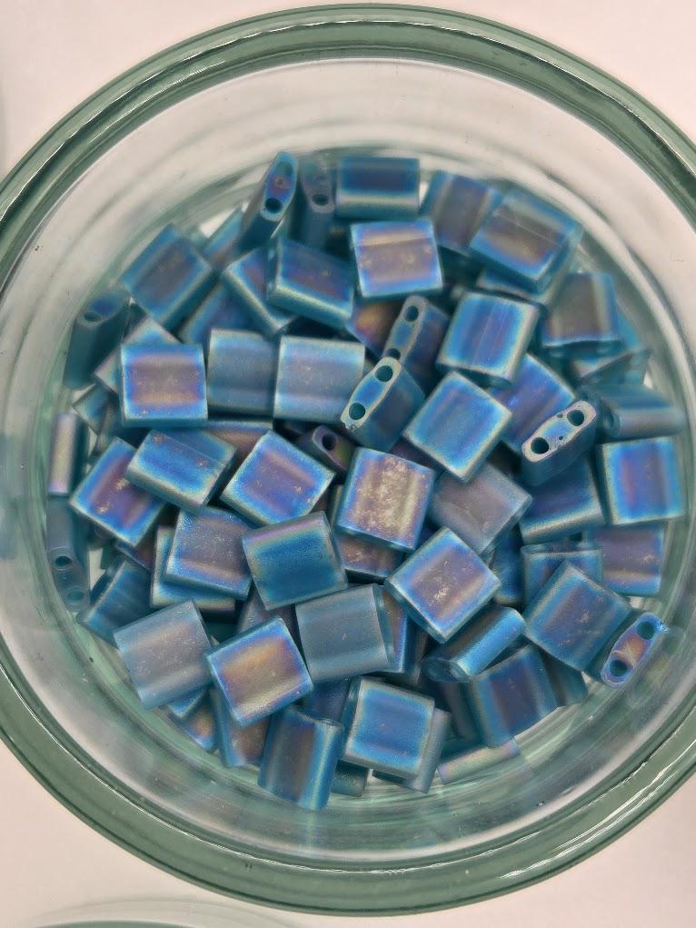 A glass jar filled with small, square-shaped blue beads.