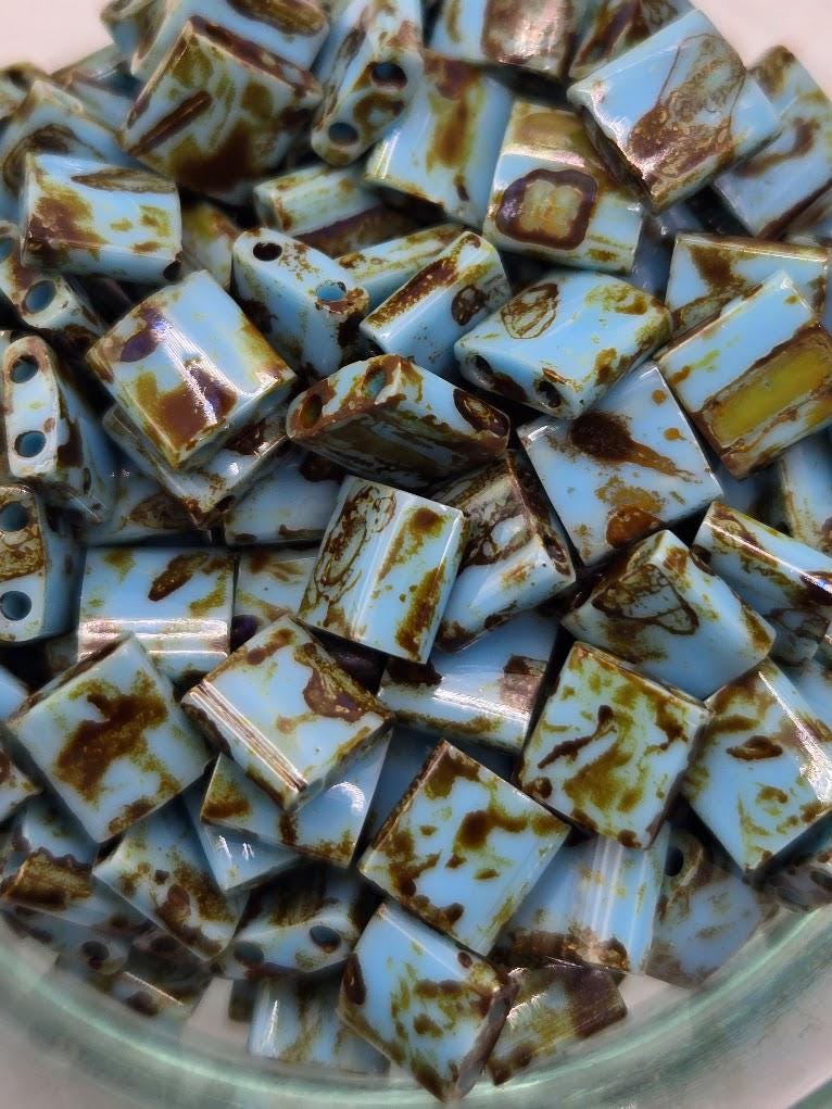 a collection of small, square-shaped blue and brown glass beads scattered on a white surface.