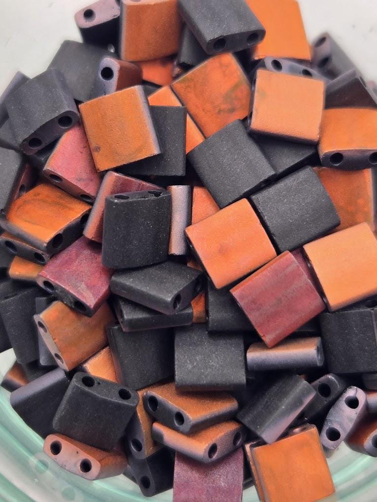a close-up view of a pile of small, colorful beads in various shades of orange, black, and purple.