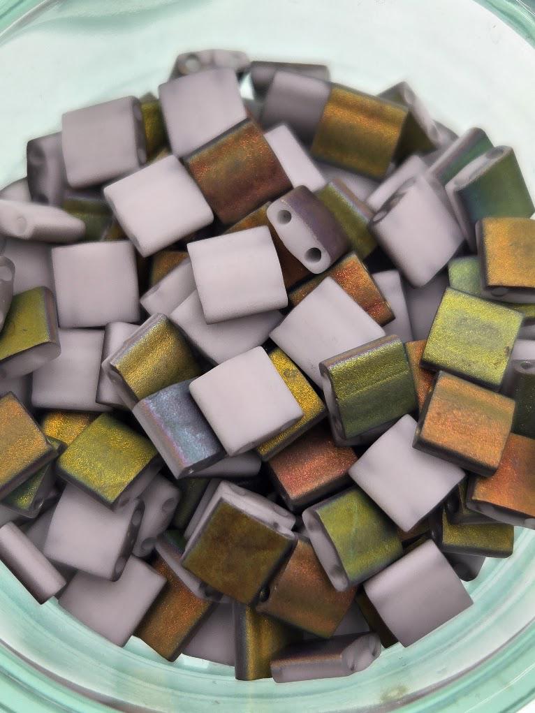 A glass jar filled with small, colorful beads in various shades of gray, green, and orange.