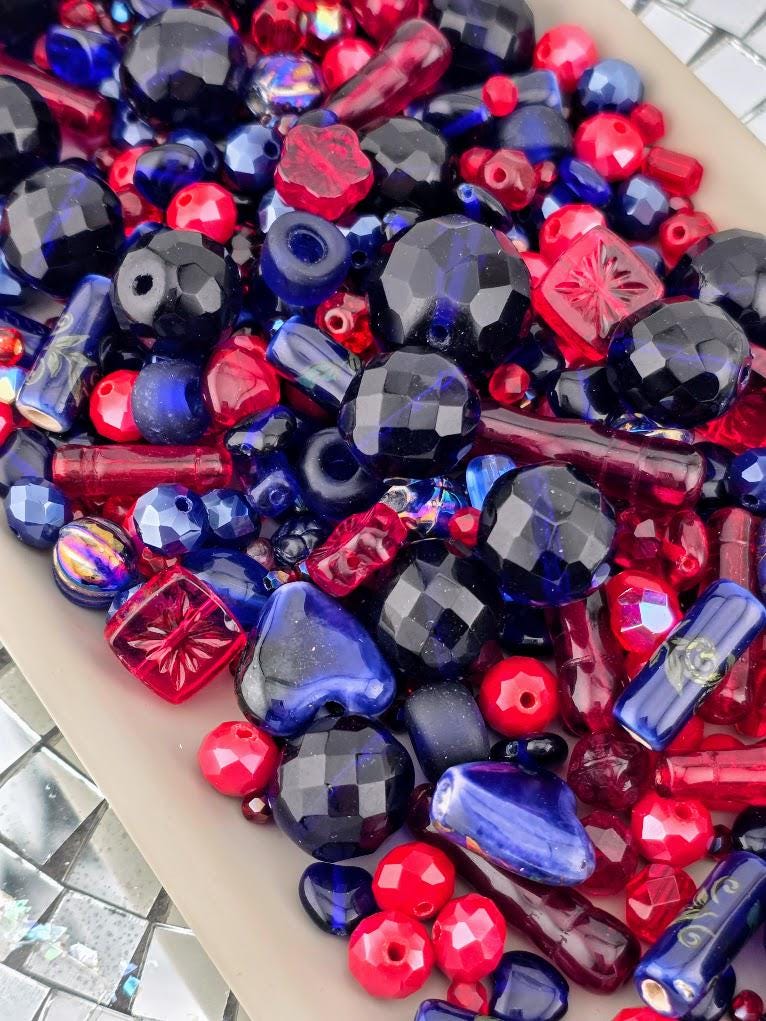 The image is a collection of various colorful beads, including red, blue, and black beads, scattered together.