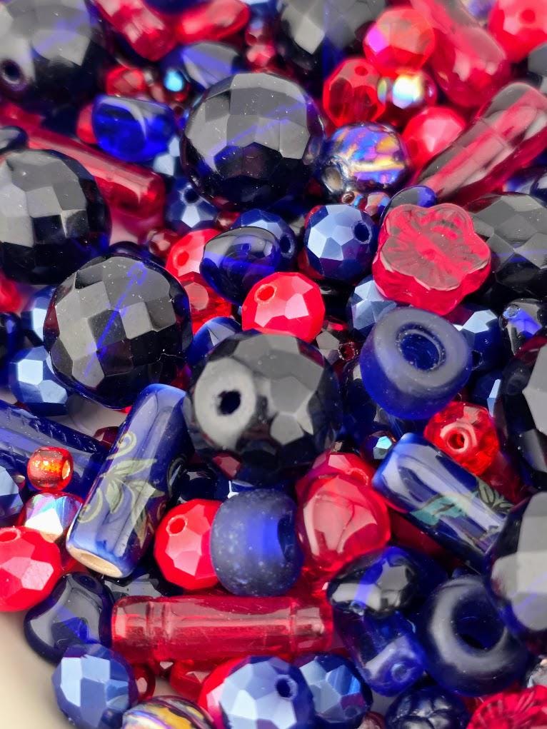 The image is a close-up of a collection of colorful beads, including red, blue, and black beads, scattered together.