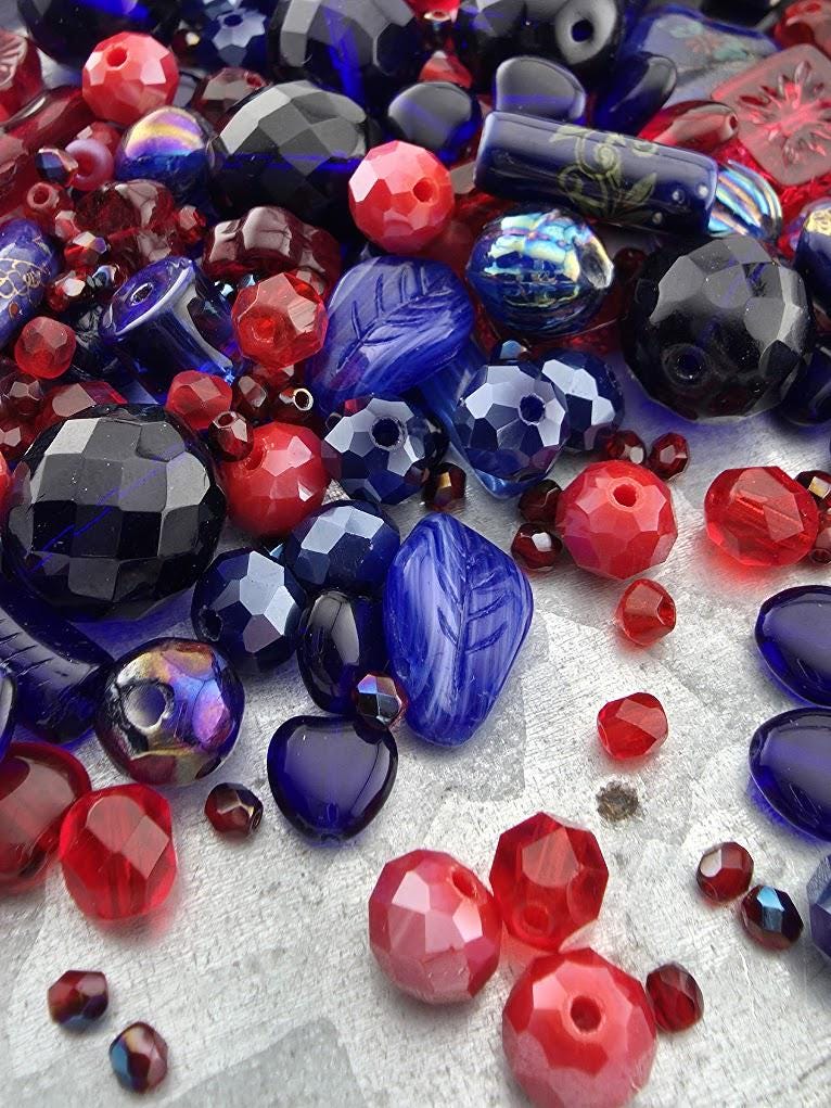 The image is a collection of various colorful glass beads, including red, blue, and black beads, scattered across a surface.