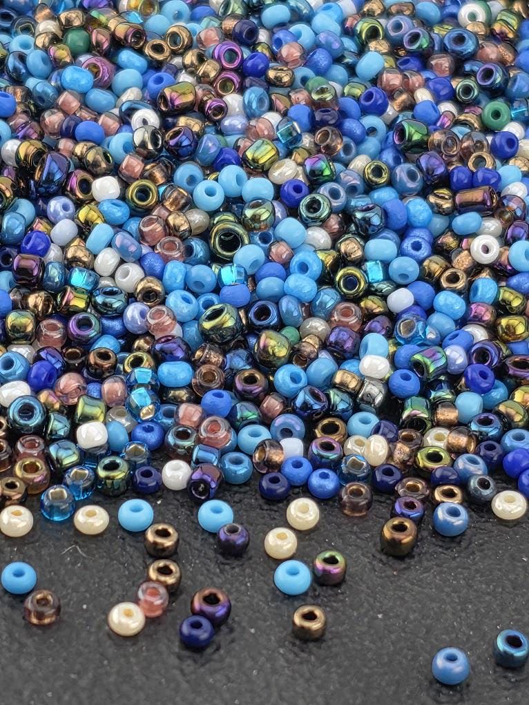 The image is a close-up of a pile of multicolored beads, including blue, purple, and gold beads, scattered on a dark surface.